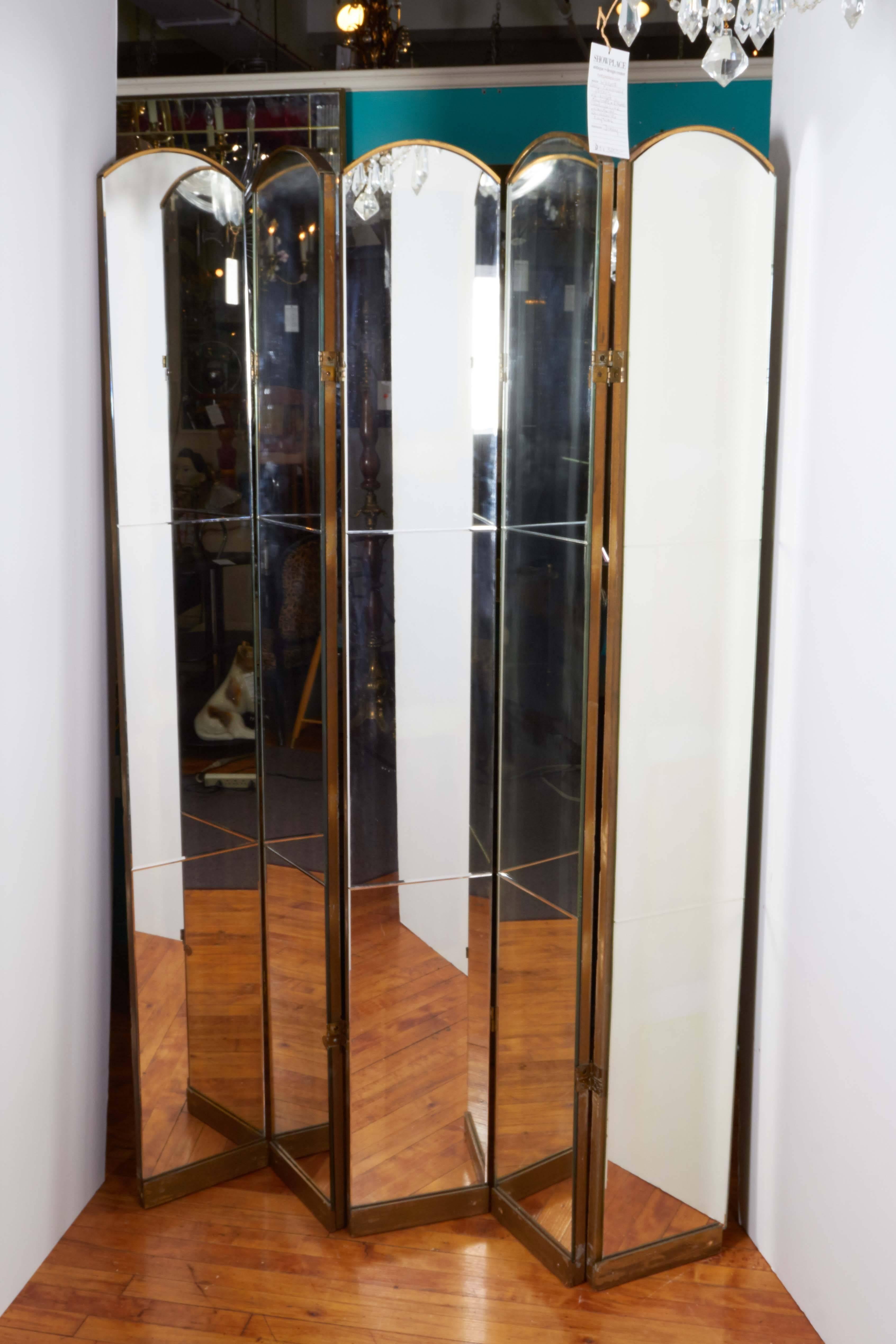 A pair of vintage folding room dividers, each comprised of five arched mirrored panels, against wood frames. Despite some presence of age appropriate wear to brass hinges, as well as some chips to glass, these room dividers remain in good overall