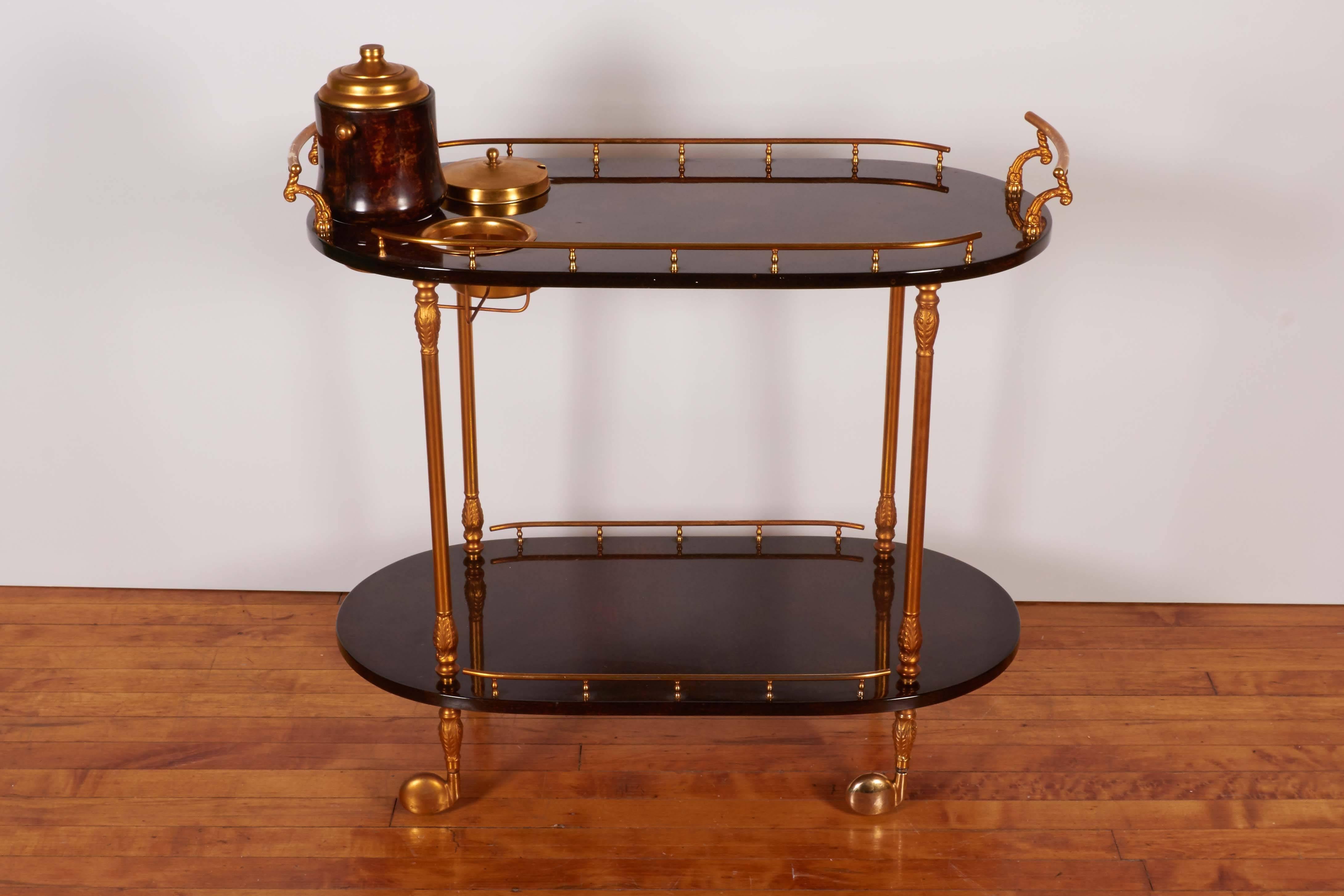 An Italian bar cart on caster wheels by designer Aldo Tura, with two galleried oval tiers in lacquered brown goatskin, with supports in the classical style, the top, flanked by handles with scroll motifs, including a bottle holder and wine cooler.