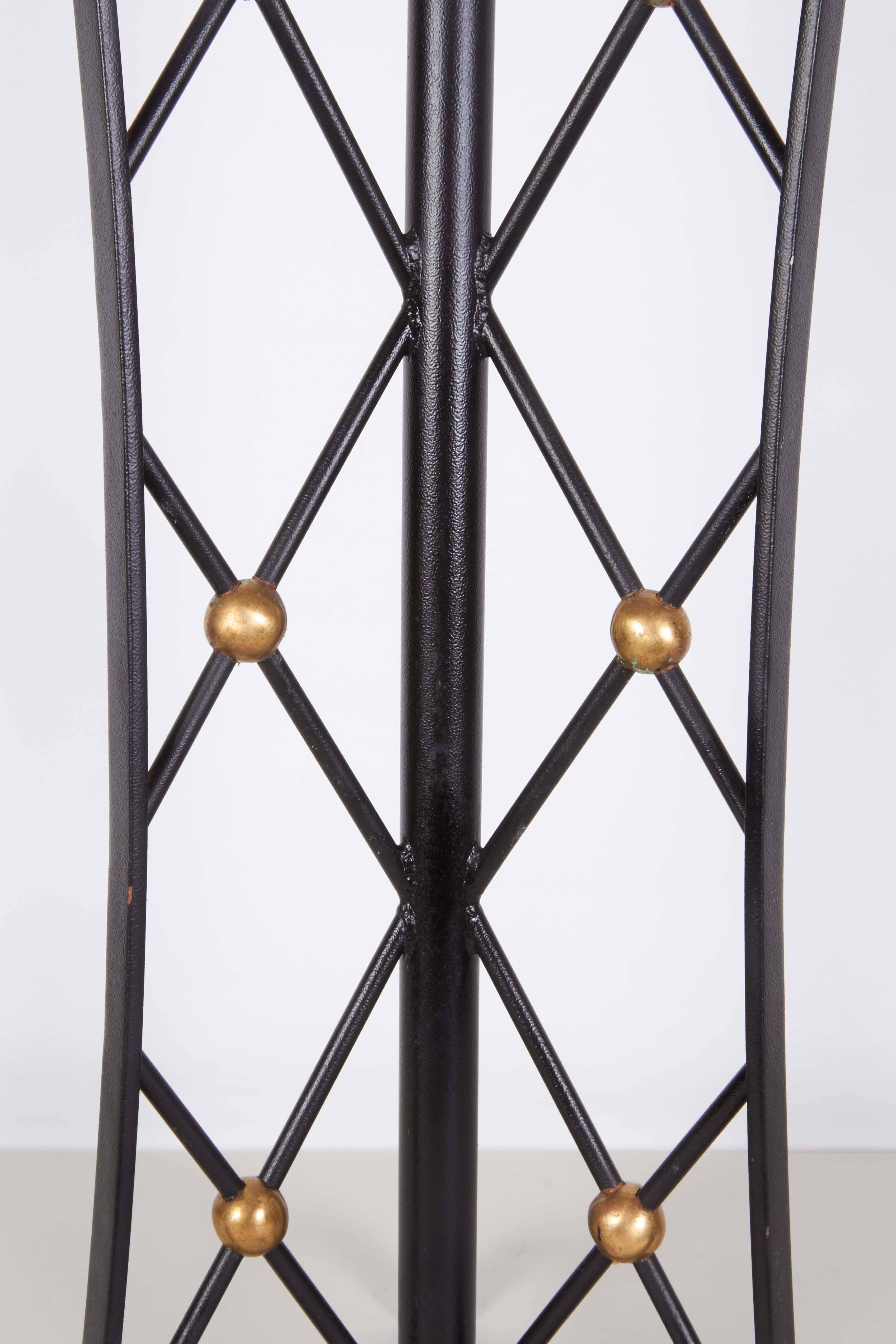 A pair of table lamps, styled after Jean Royère's signature 'Tour Eiffel' designs, in black painted wrought iron, with three panels of lattice brackets (otherwise 'croisillons'), with intersecting brass-plated accent balls, on tripod legs. Each