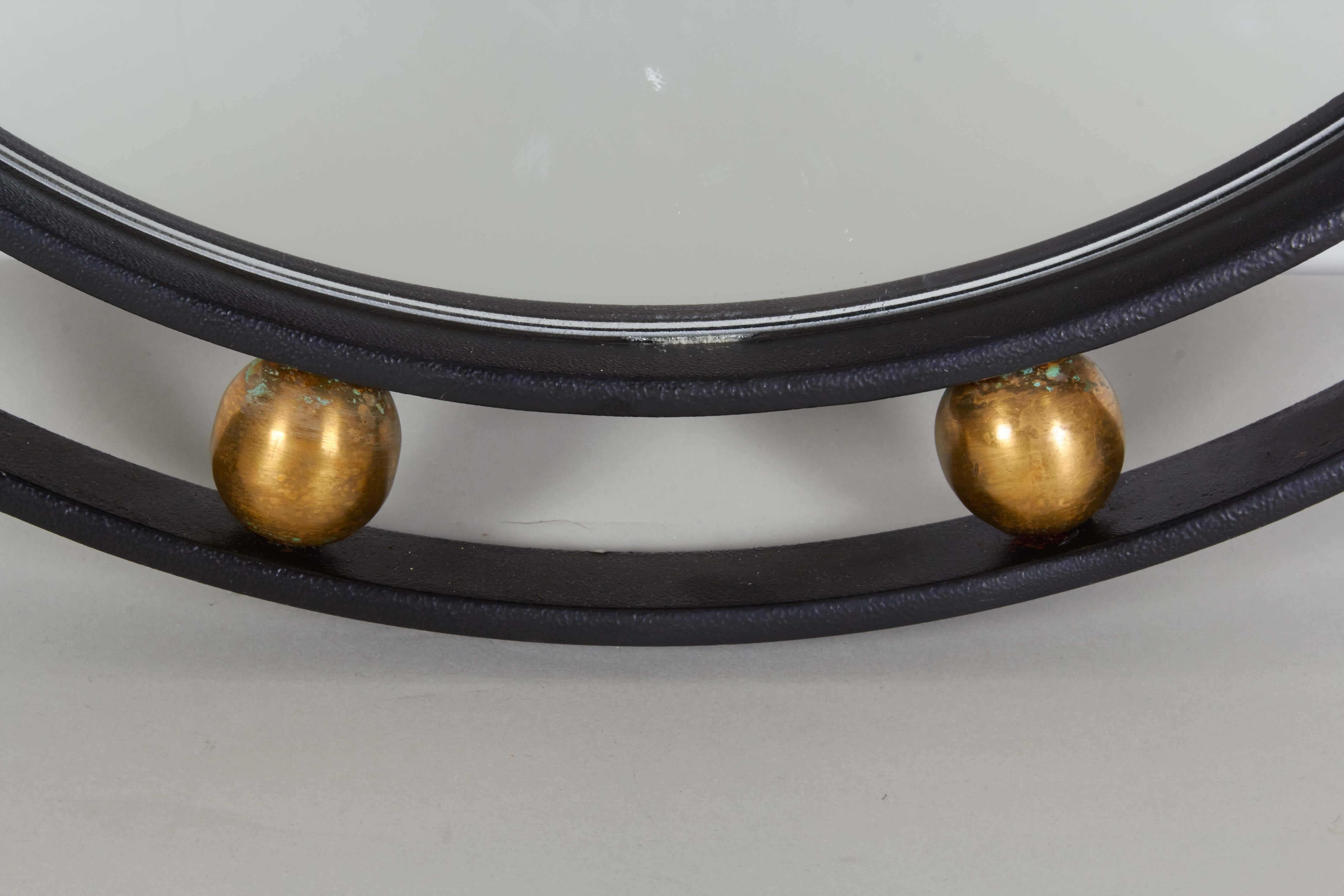 A round wall mirror in French Modern style, the glass set against a frame crafted of black painted wrought iron, accented with brass balls. Good condition, consistent with age and use.

10776.