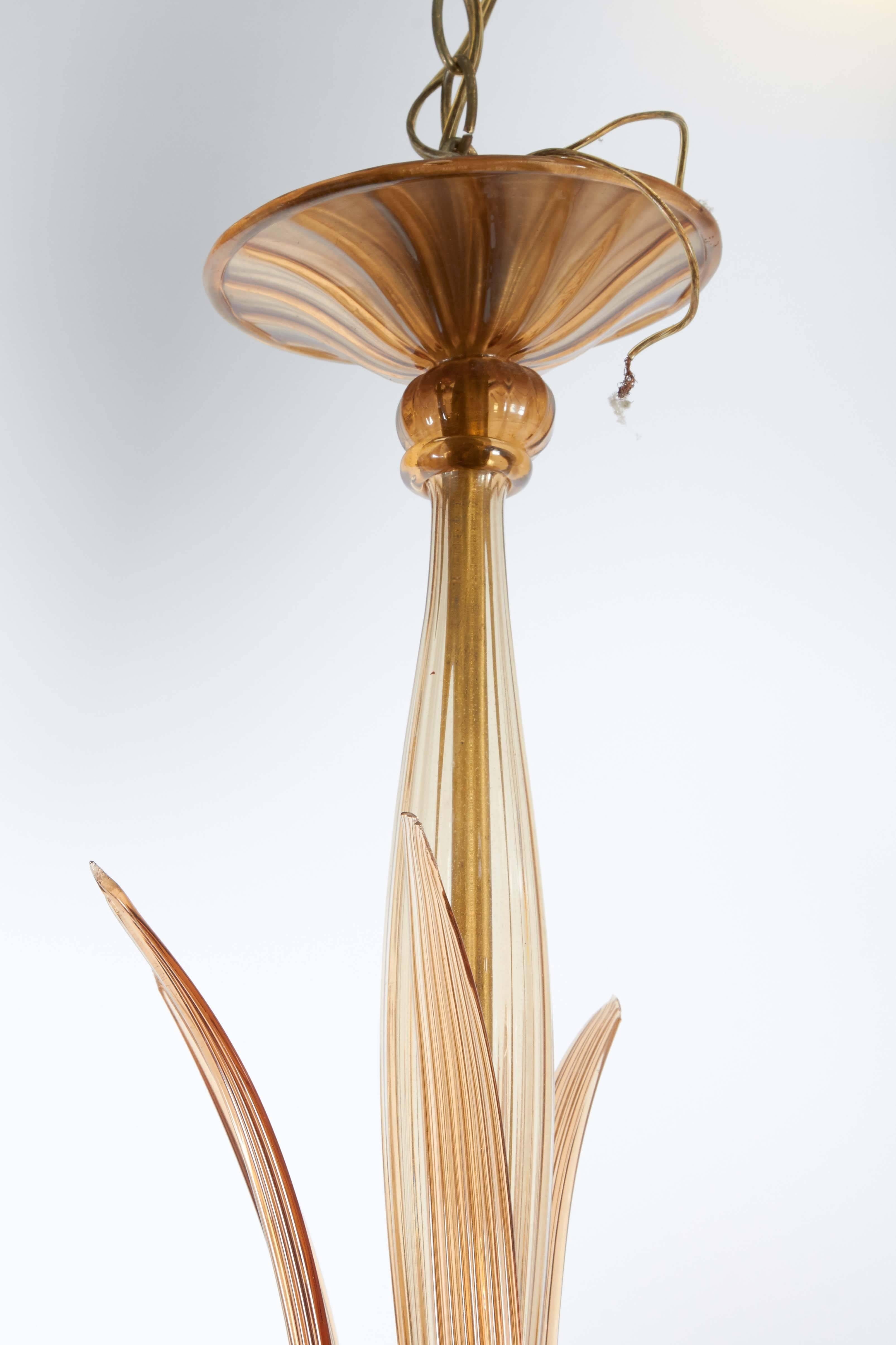 A vintage chandelier entirely in ribbed amber toned Murano glass, with five scroll arms, each supporting trumpet-form bobeches, with decorative palm leaf stems, extending from centre. Despite loss of one palm leaf, this light fixture remains in very