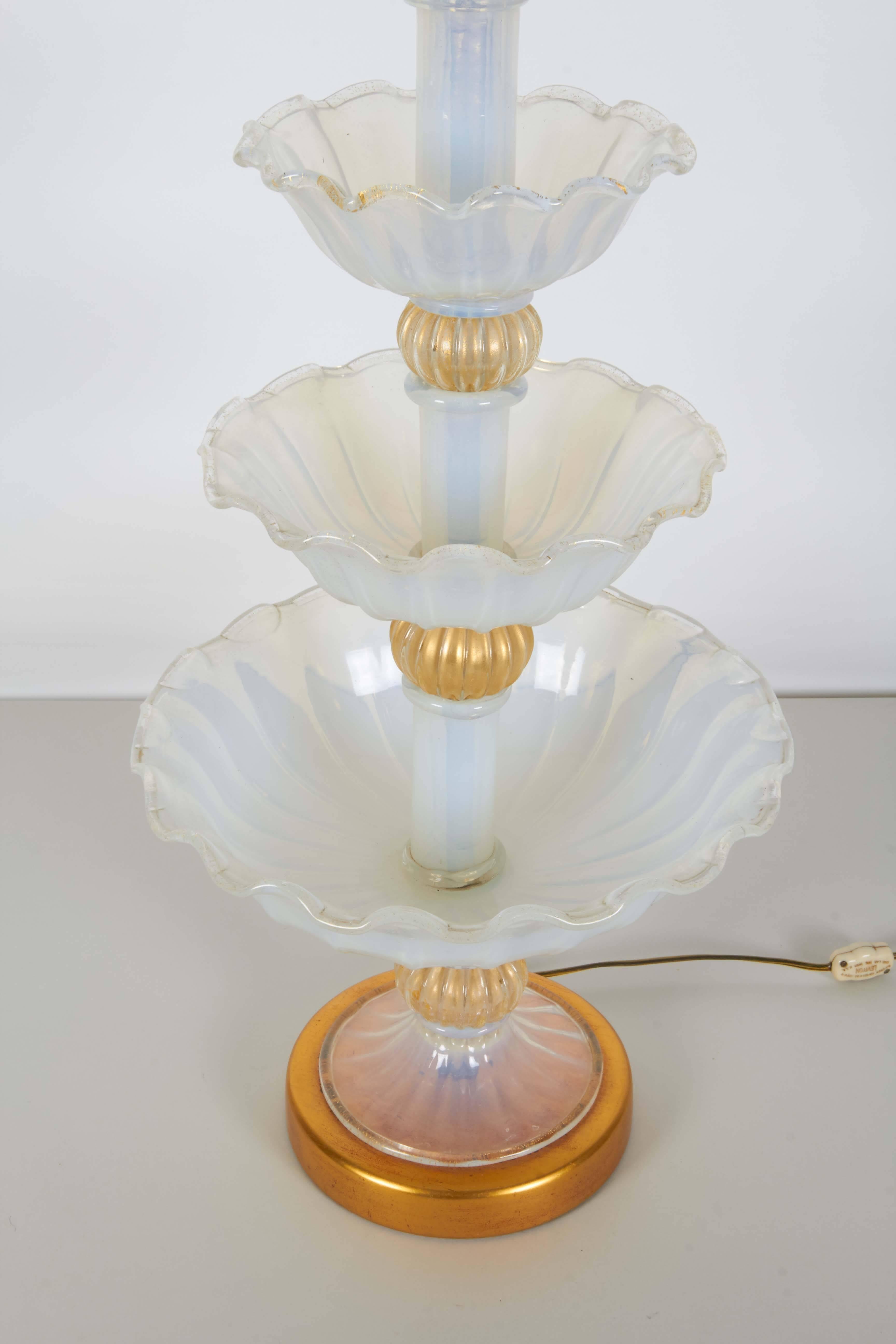 An impressive table lamp in opalescent Murano glass by Seguso, manufactured circa 1950s, with three graduated levels of handblown bowls with ruffled edges, accented with four gold leaf ribbed bulbs, on circular gilt metal base. Wiring and double