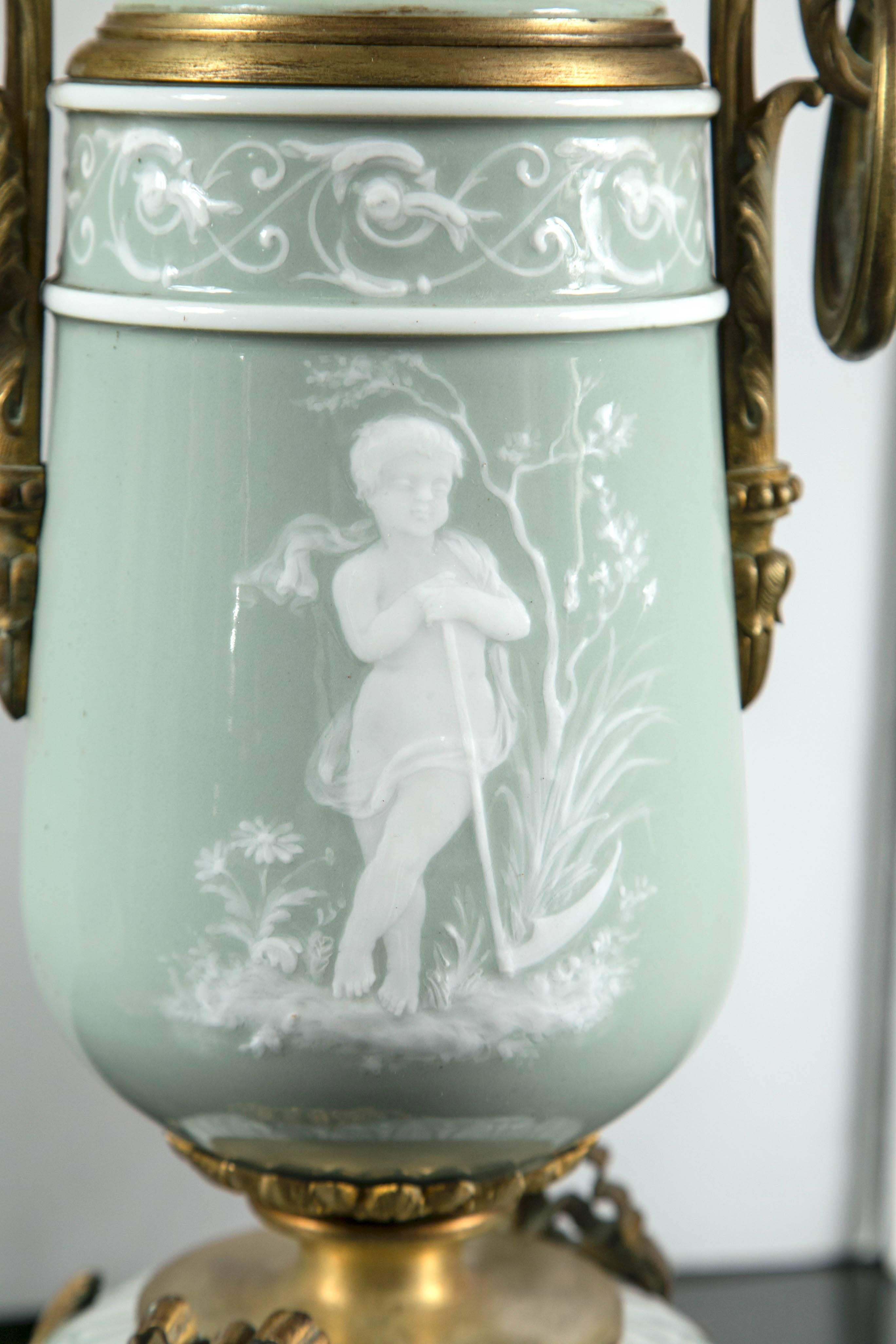 This pair are of pale green and white glass, with gilt bronze mounts. Decorated on front and back sides with children in different poses. The original burner sits atop. Then scrolling feet with acanthus leaves on two and a medallion with ribbon on