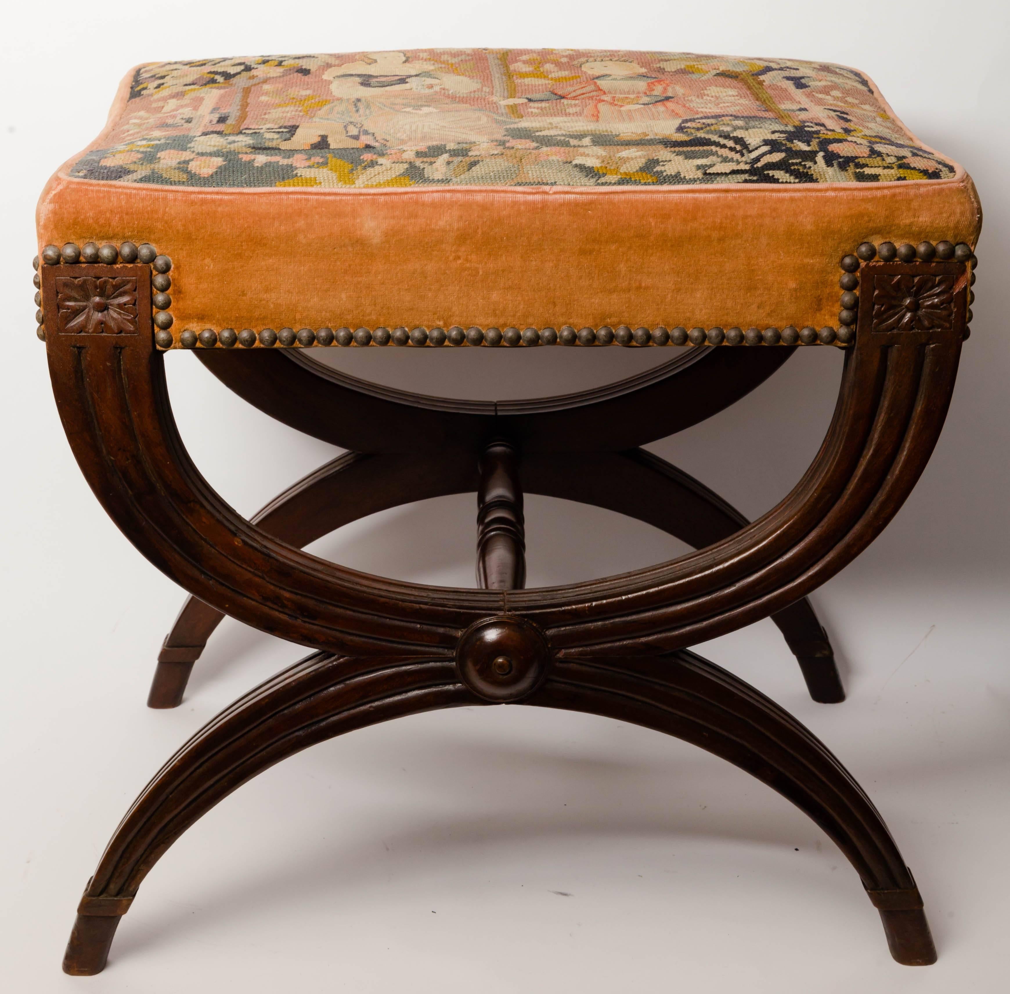 French Empire style mahogany Curule base stool with needlework top. Depicting a medieval lady and a page in a wooded setting. The base has rectangular rosette at the top of each leg. The Curule base is reeded with a turned disc at the joining. The