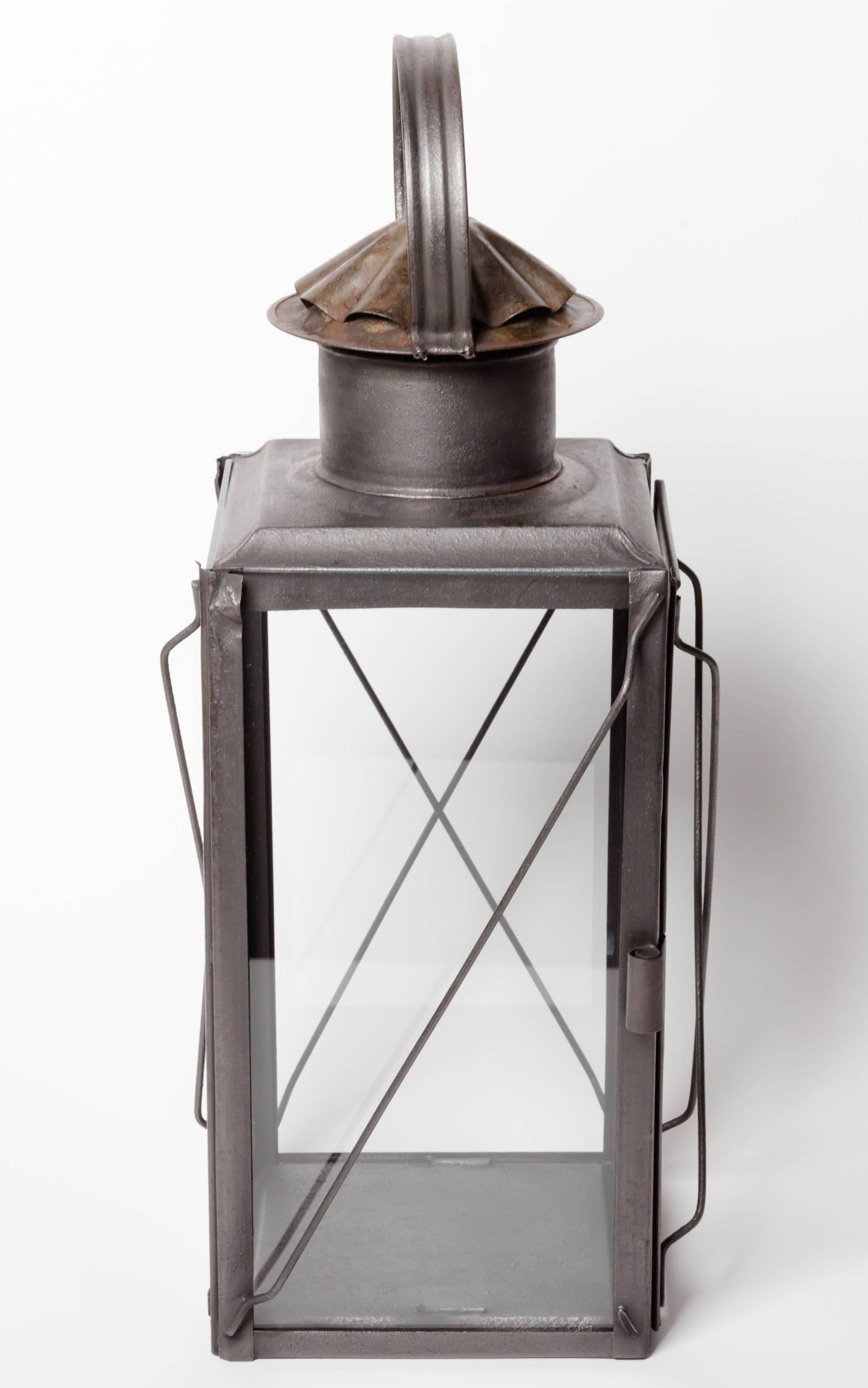 This beautifully simple 19th century Scottish glazed gunmetal finish steel lantern has a circular ribbed handle above ruffled vent cap. One side is a door with a spring coil door clasp. Steel rod X design guards are on the outside. The lantern was