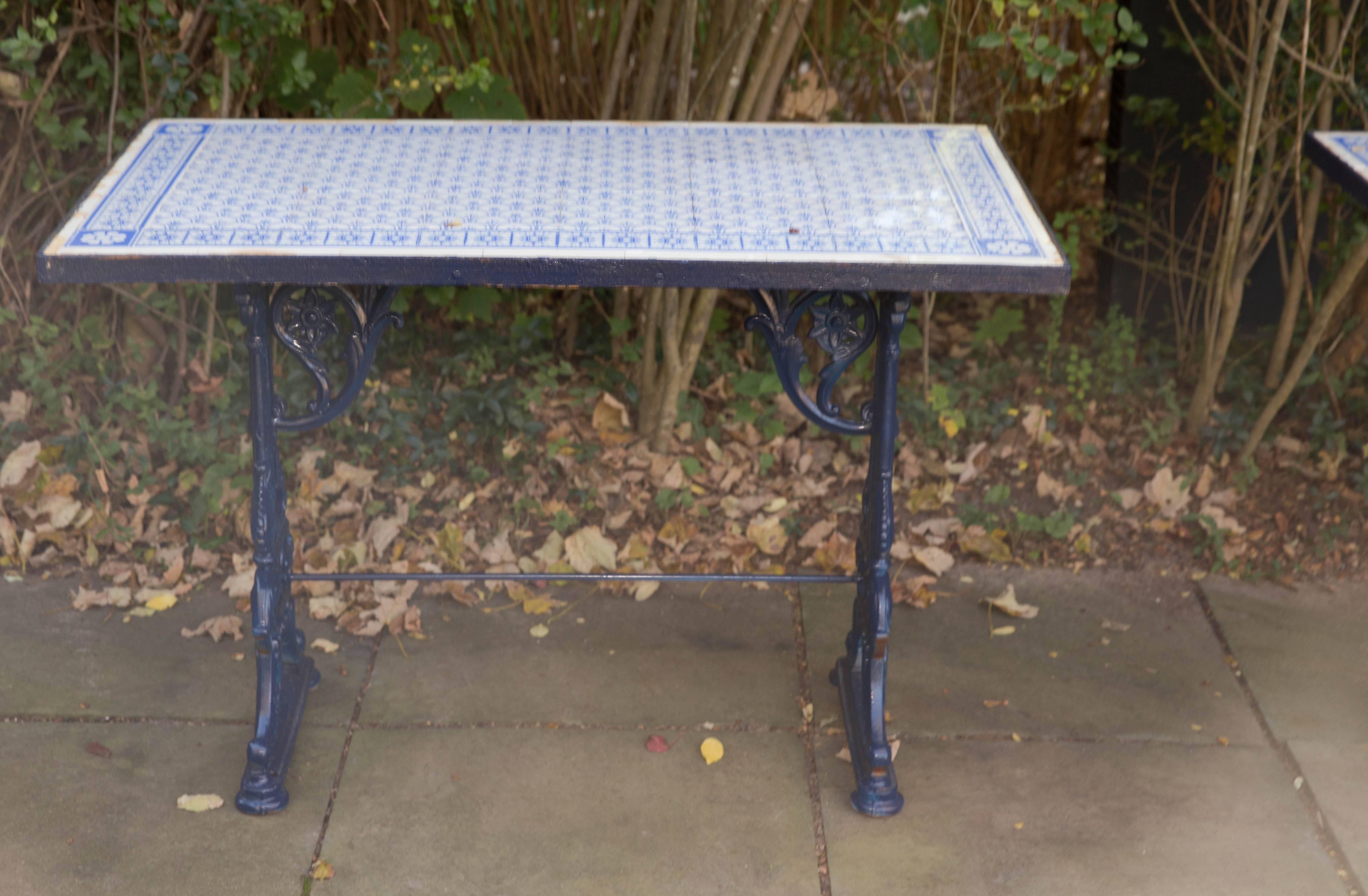 Pair of English Victorian blue painted cast iron pub table consoles in the aesthetic taste with Spanish or Moroccan blue and white tile tops. The base has flower motif support brackets. The tops are iron bound cement with inlaid tiles. The tiles