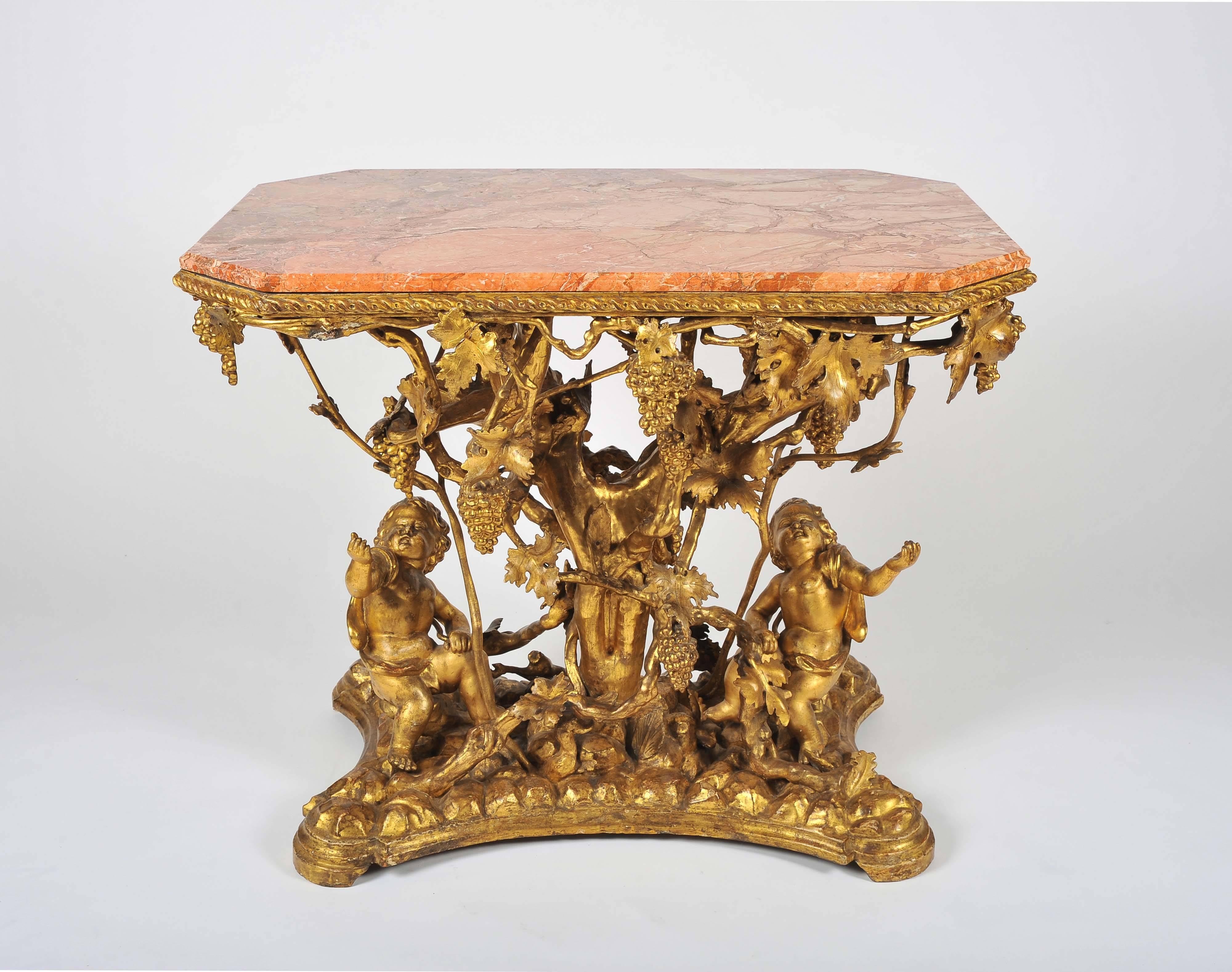 An extraordinary console or centre table, the base with carved wood and gilt gesso formed of Bacchanalian putti amongst a vine with branches, leaves and bunches of grapes, on a simulated rocky ground. The gilding a wonderful warm gold, slight rubbed