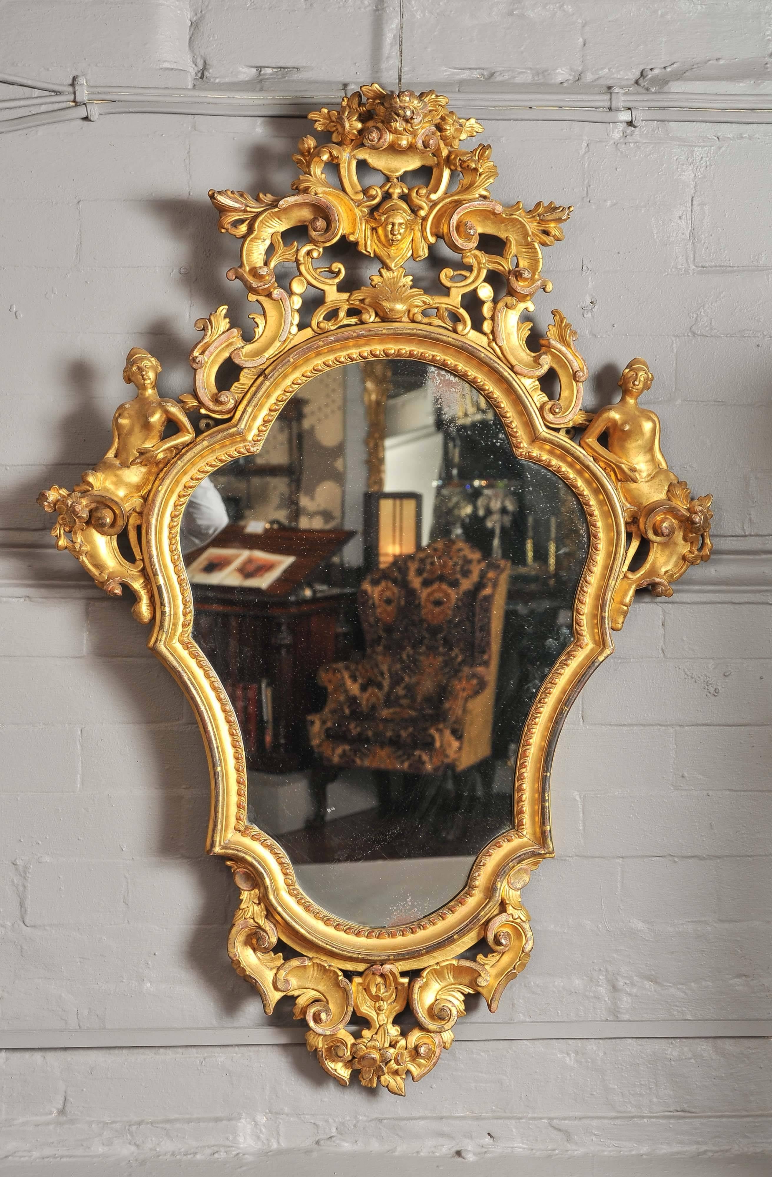 The shaped frame with profuse carving top and bottom containing figures, masks, flowers and scrolls.
This beautiful example with rich gold color retains its original gilding and glass plate.