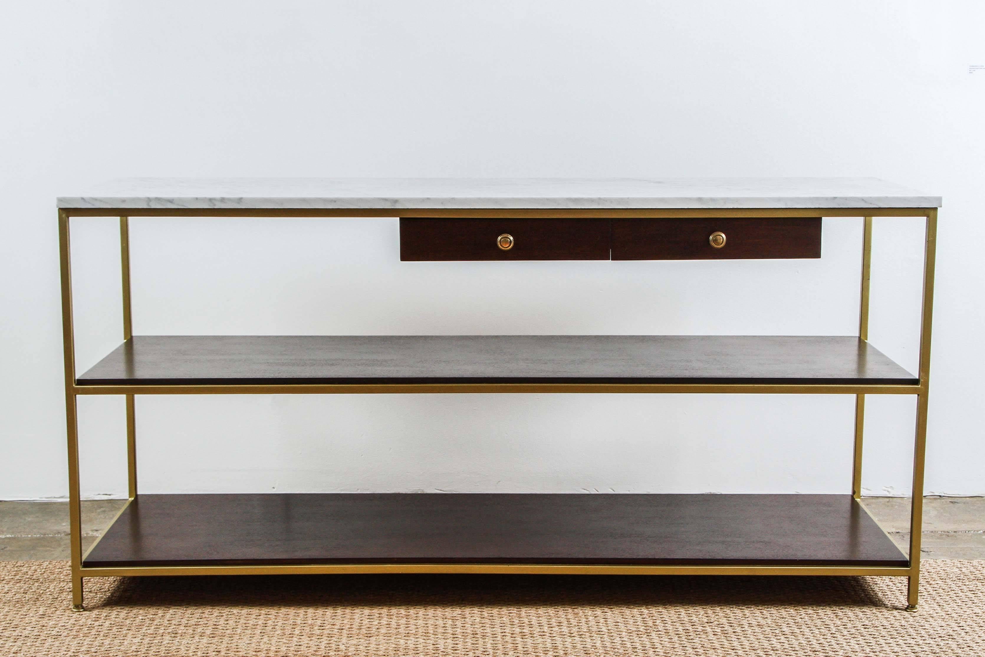 A vintage console, designed by Paul McCobb and produced circa 1950s by Calvin Furniture Co., with white marble top on brass frame, with two exterior drawers, each with brass knob pulls, over two wood shelves. Markings include original label [Calvin,