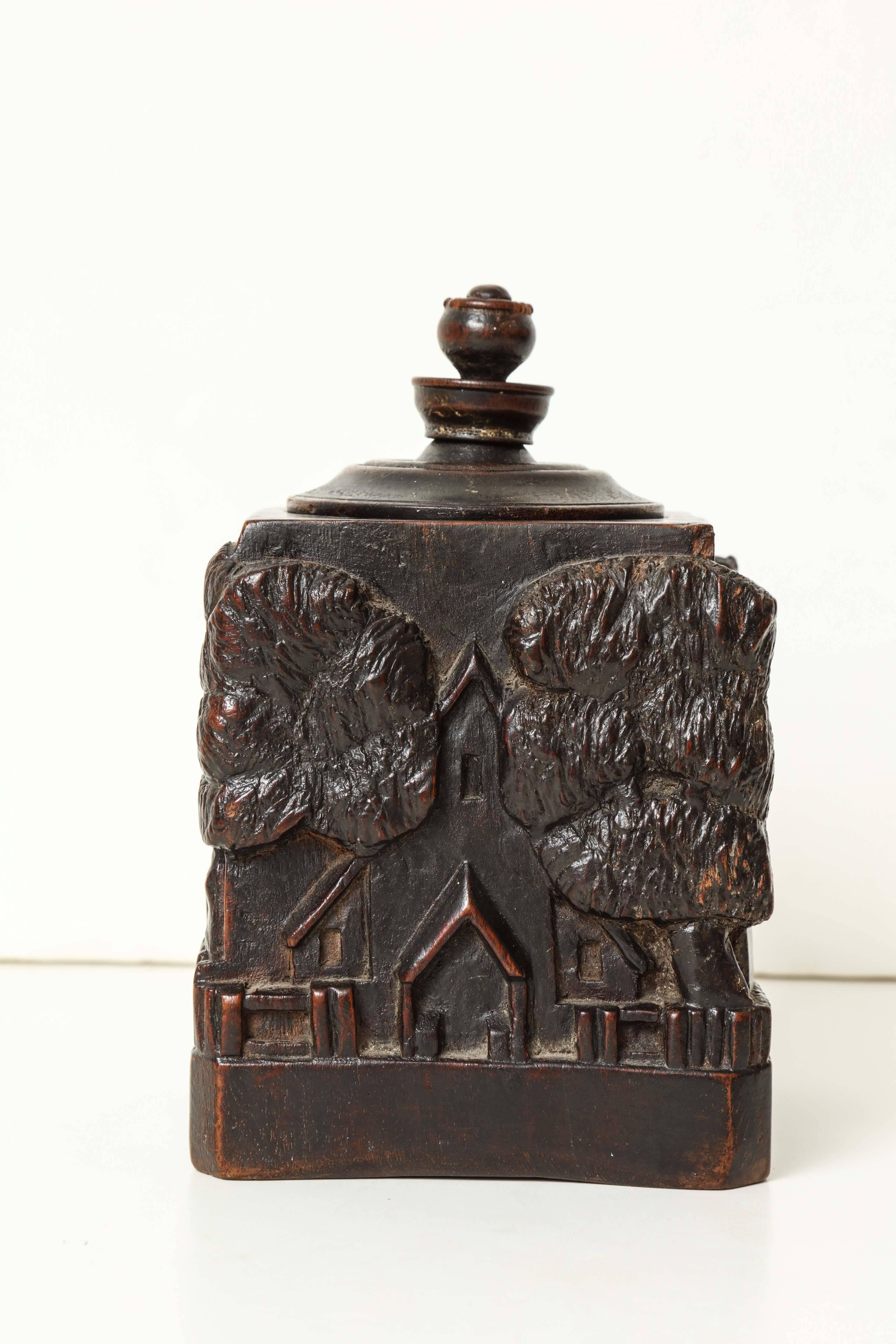 An unusual 18th century stained walnut tobacco jar
carved in relief with a castle, church, cottages and trees in high relief
with a turned lid
possibly Irish, circa 1750.
 
