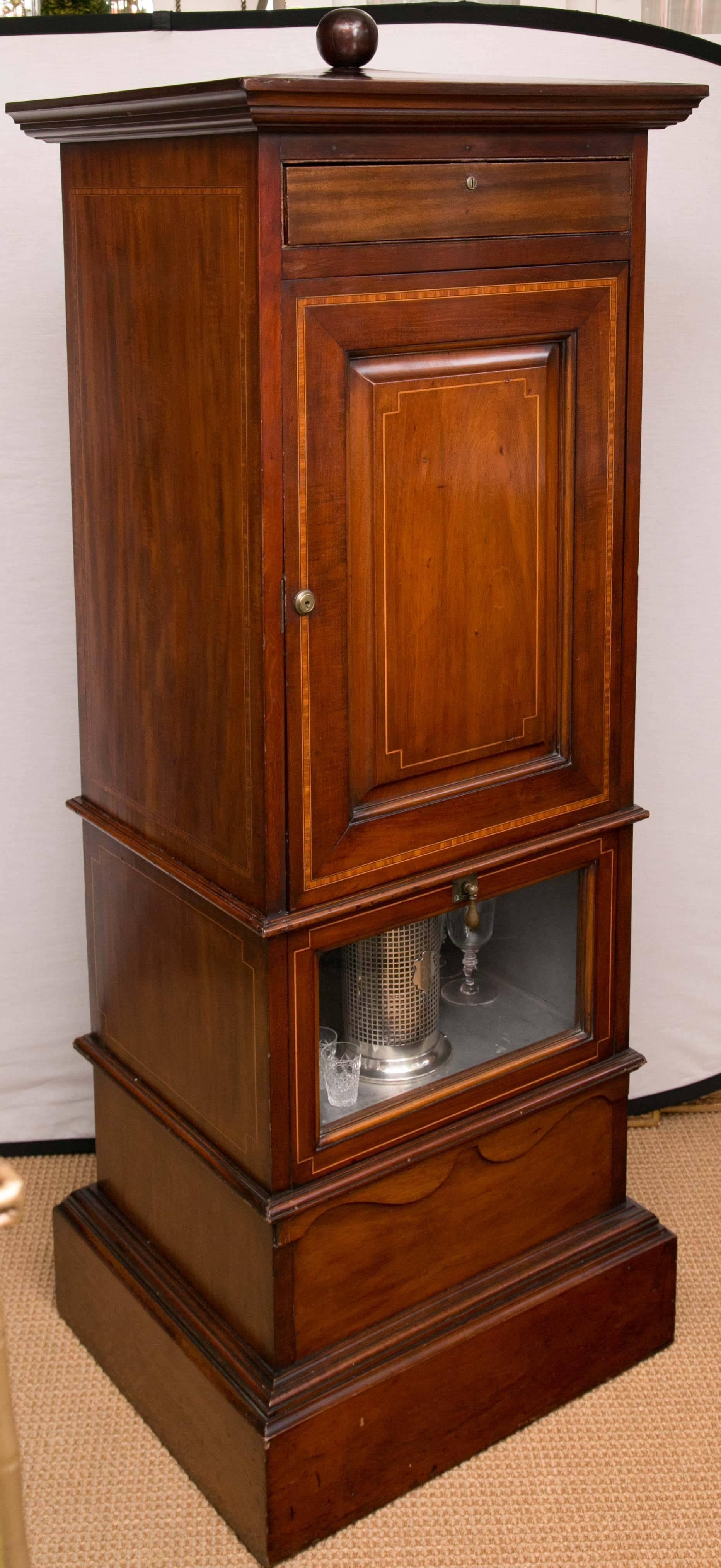 A tall, obelisk form dry bar. The top drawer holds a variety of vintage game pieces, the center door reveals two pull out shelves, including decanters, glasses and barware and sterling silver. The lower glass door opens to a humidor. All of solid