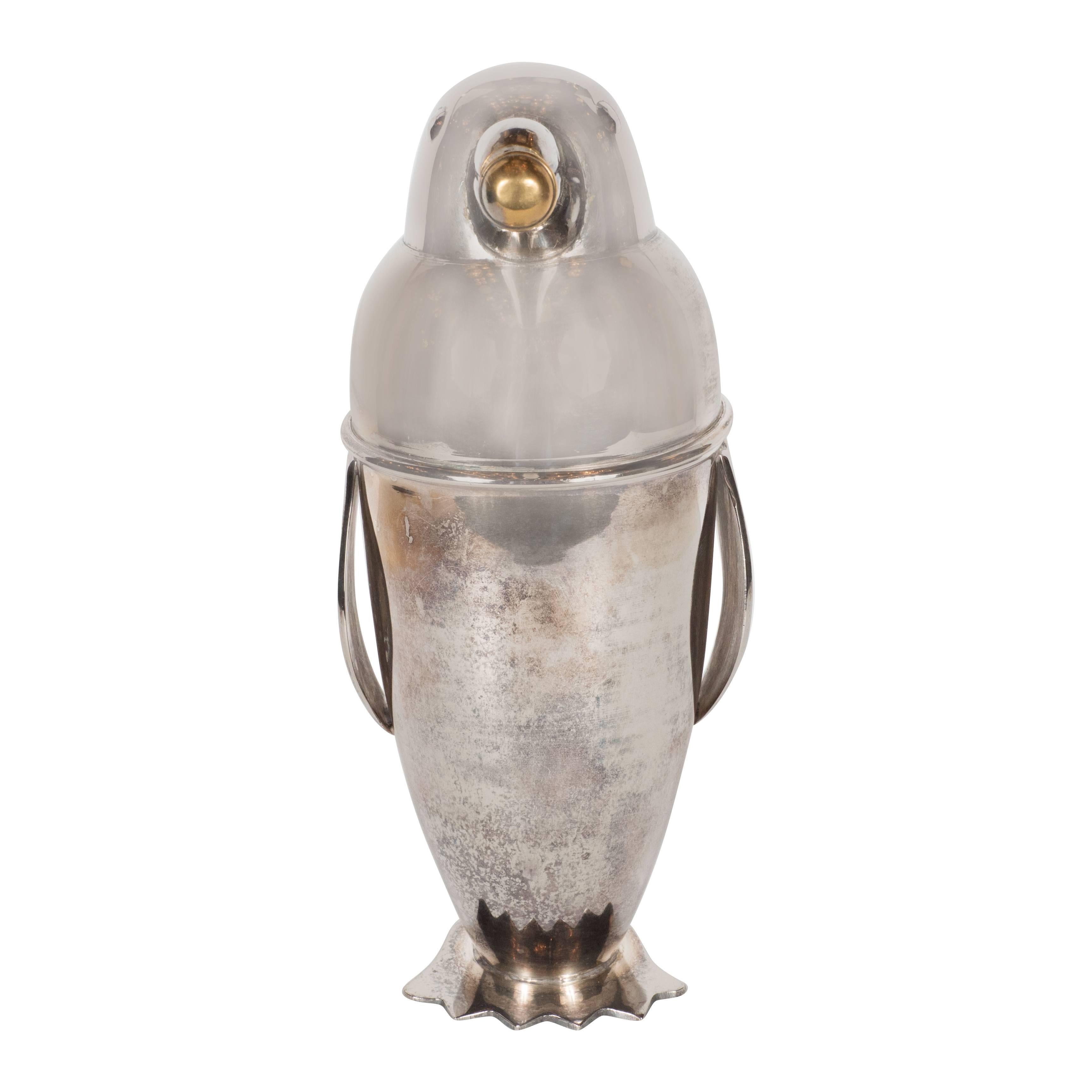 A silver plate Art Deco style cocktail shaker in a stylized penguin form with a handle, the beak (complete with a brass stopper) forms a spout from which you would pour your drink and penguin feet at the base for support. The Shaker comes in two