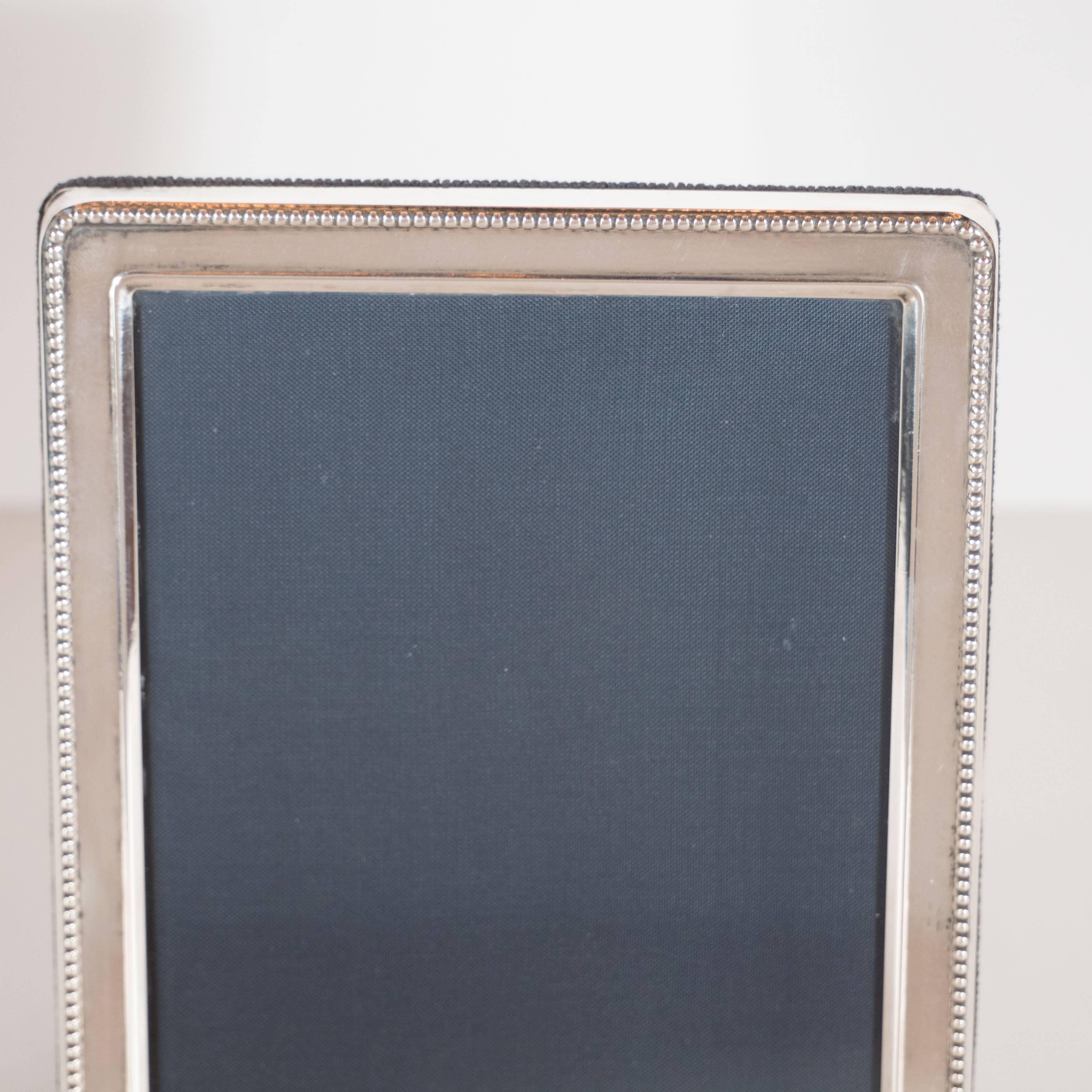 A Mid-Century Modernist sterling silver photo frame features fine beading repeating around the perimeter. The back is lined in navy felt with sterling fittings. It is designed to hold a 5" x 3.5" photo. It can be displayed either