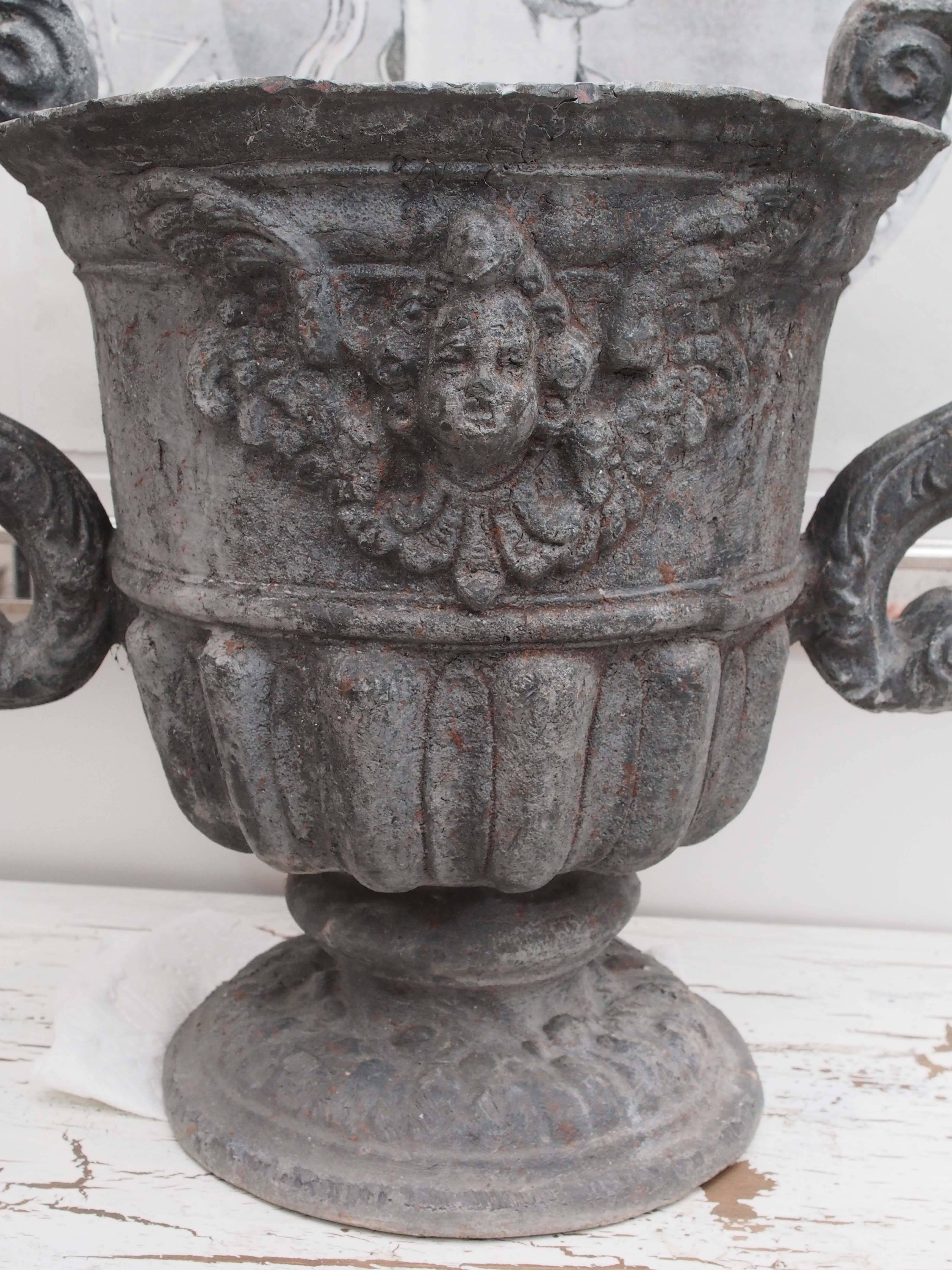 A rare and unique set of four matching large lead urns with S scroll arms and cherub decoration. In great condition.