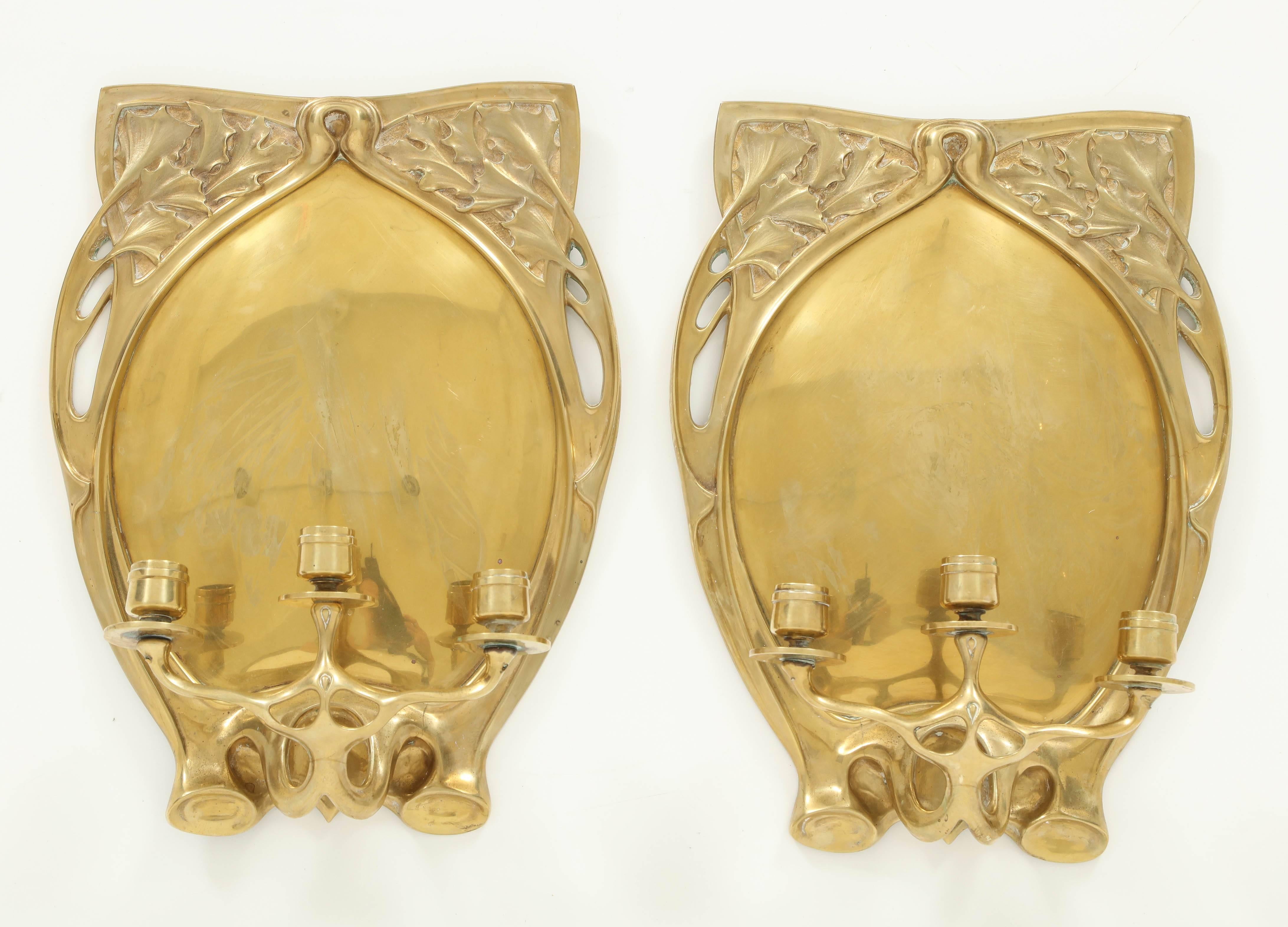 Pair of heavy cast brass three-arm candle sconces with attached hand-forged reflective brass backplate. Continental, probably Belgian or French, circa 1900.