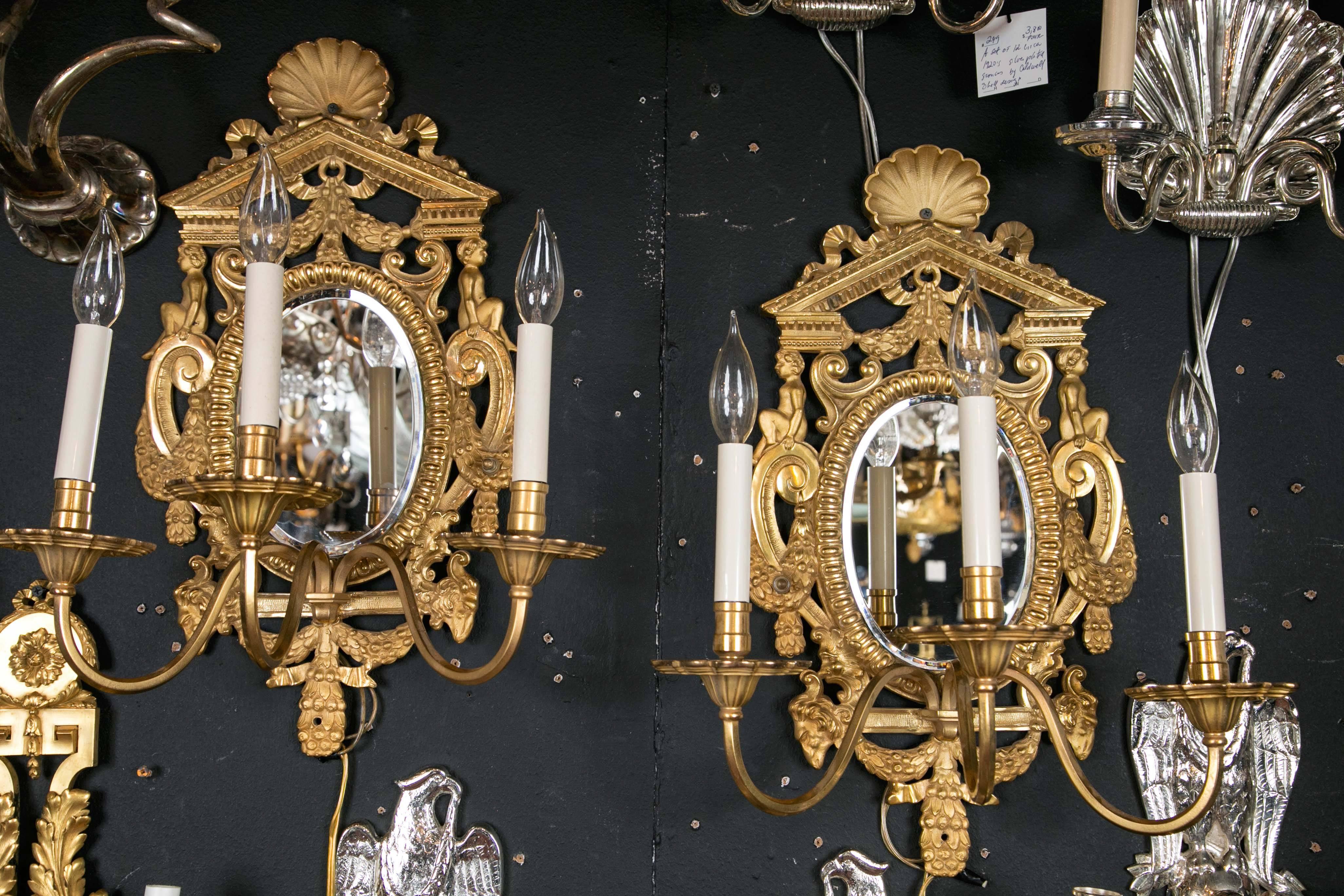 A pair of gilt bronze Caldwell sconces in the neoclassical style with mirrored backplates, circa 1900.