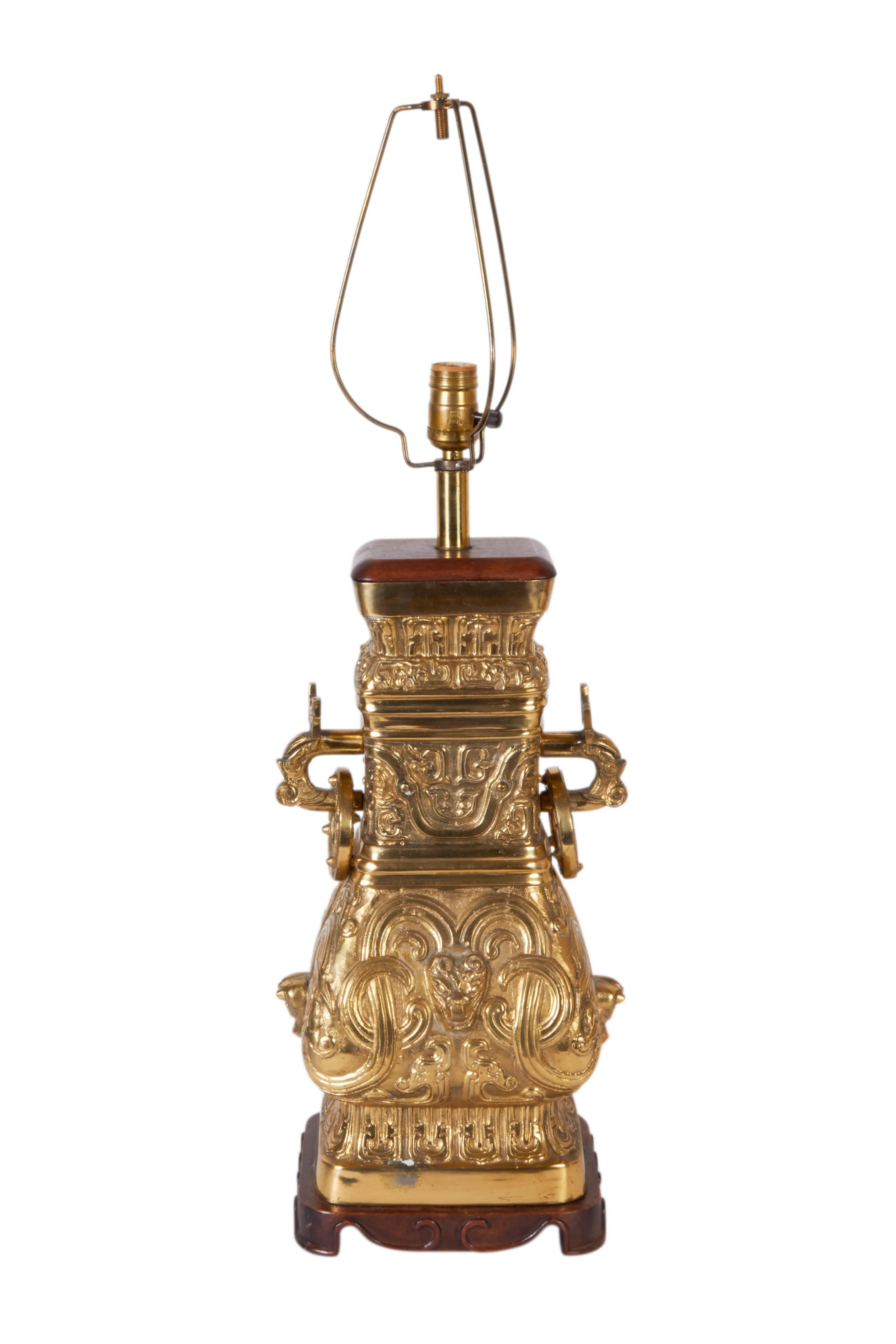 A pair of vintage table lamps in the manner of designer James Mont, with single sockets on brass square baluster form bodies, styled after handled archaic Chinese vases, with wood mounts and serpentine bases. Markings include [Made in Hong Kong]