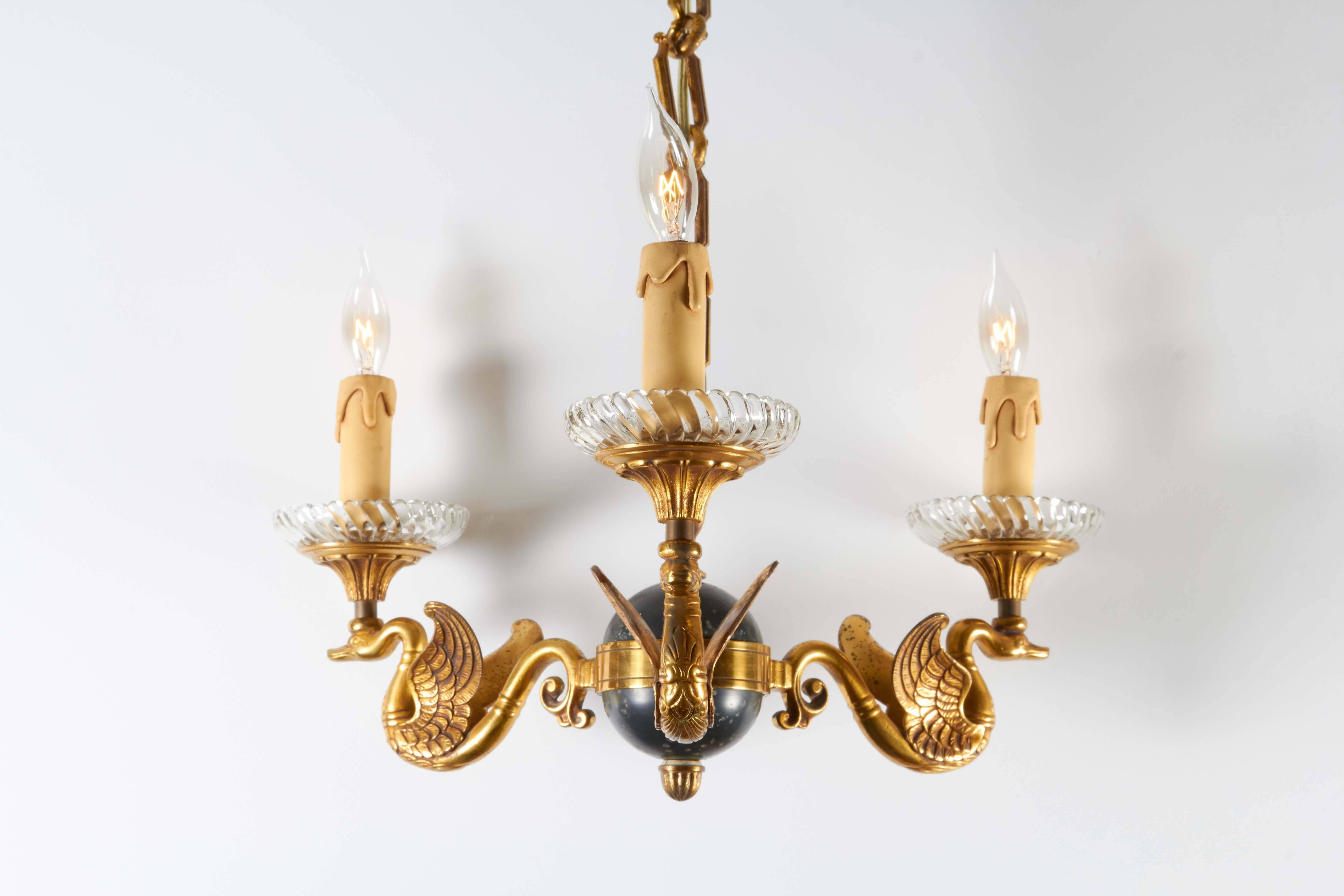 A 1940s Italian chandelier, designed in the Empire style, with black celestial globe, supporting three scrolling brass arms with swan motif, each topped with ribbed glass bobeche and faux wax candle socket covers, suspended by original heavy chain