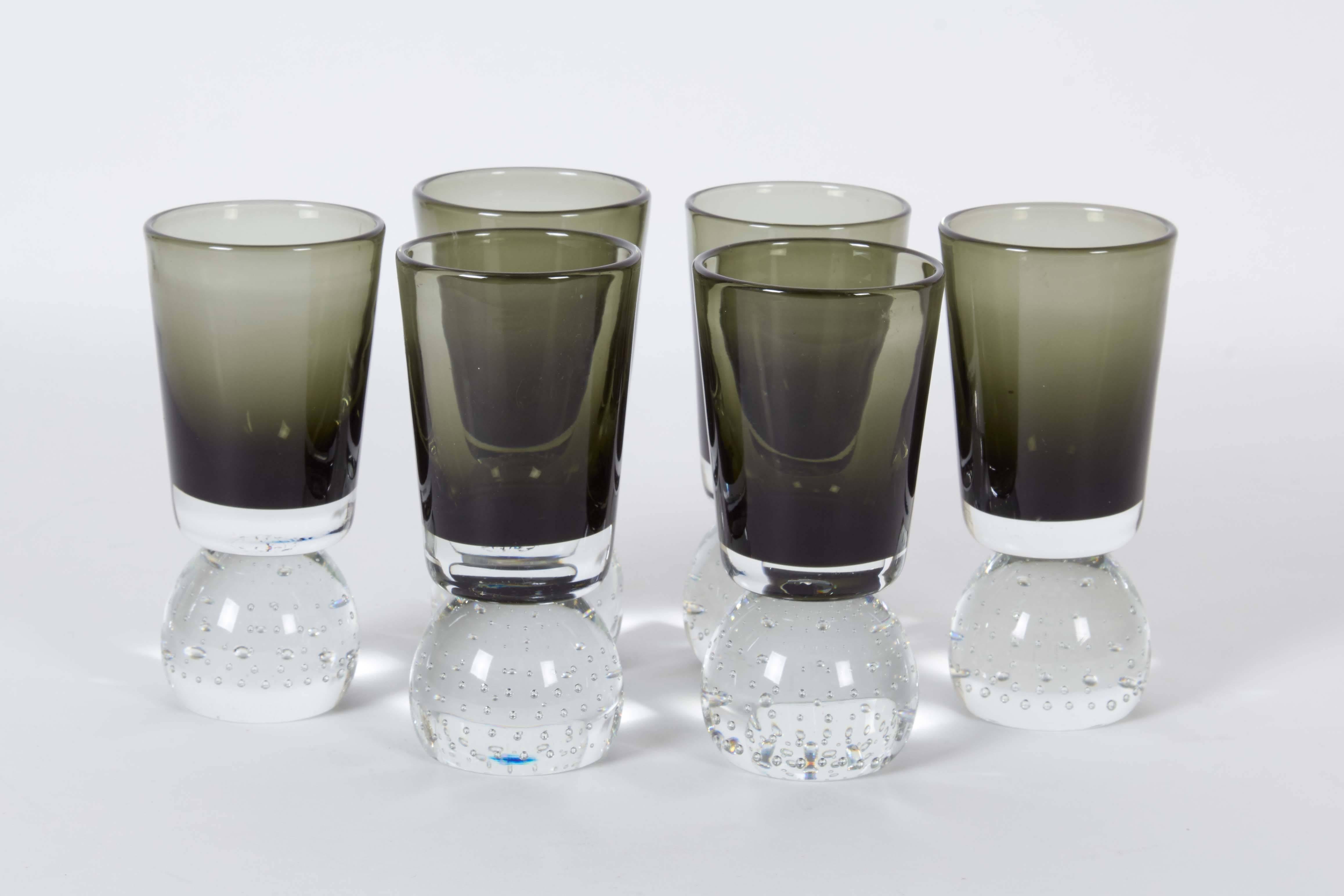 A set of six glasses, manufactured in the United States, circa 1950s by Swedish-born glass maker Carl Erickson, vessels in smoked blown glass, each on clear round bases with controlled bubbles. The set remains in excellent vintage condition,