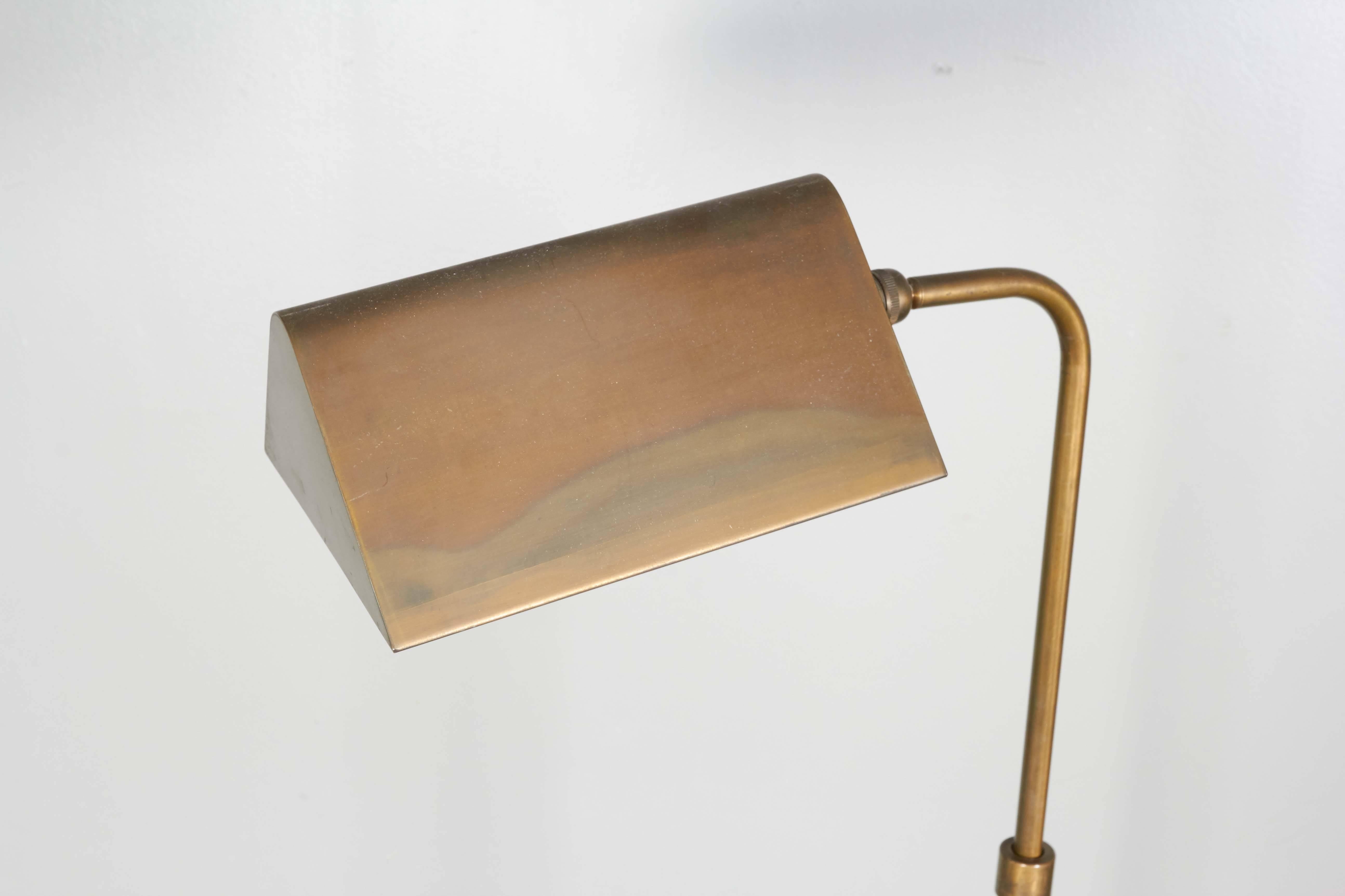 A circa 1960s floor lamp in brass, tent shade with rounded corners and white enamel interior, raised on curved stem and round base. The lamp remains in good vintage condition, with age appropriate patina and minor spots to brass, some wear to enamel