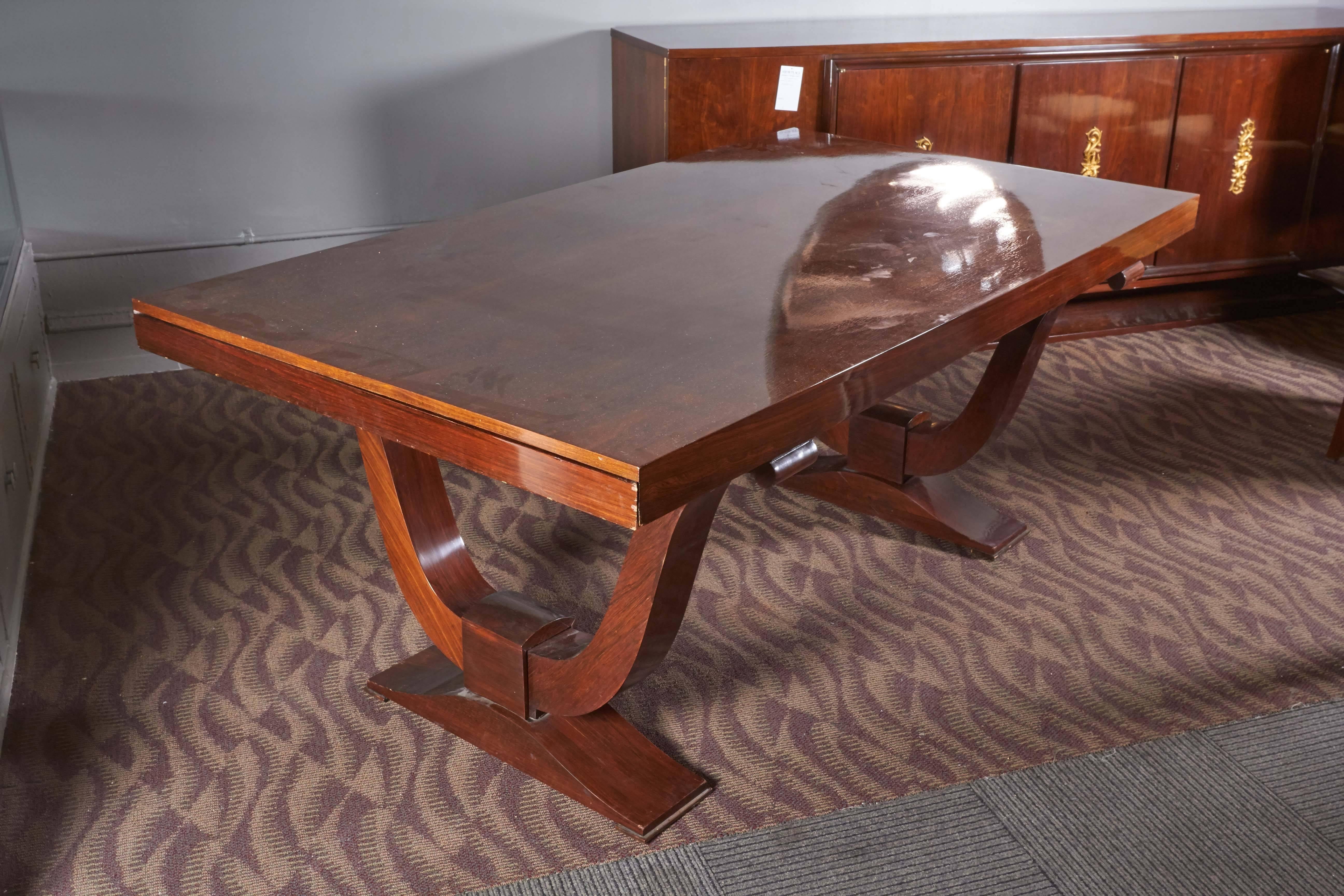 An Art Deco era mahogany dining set by French designer Jules Leleu, produced circa 1940s, comprising a dining table with extending top on two u-form pedestal bases, with set of eight chairs (six side/two arm), with upholstered backs and seats on