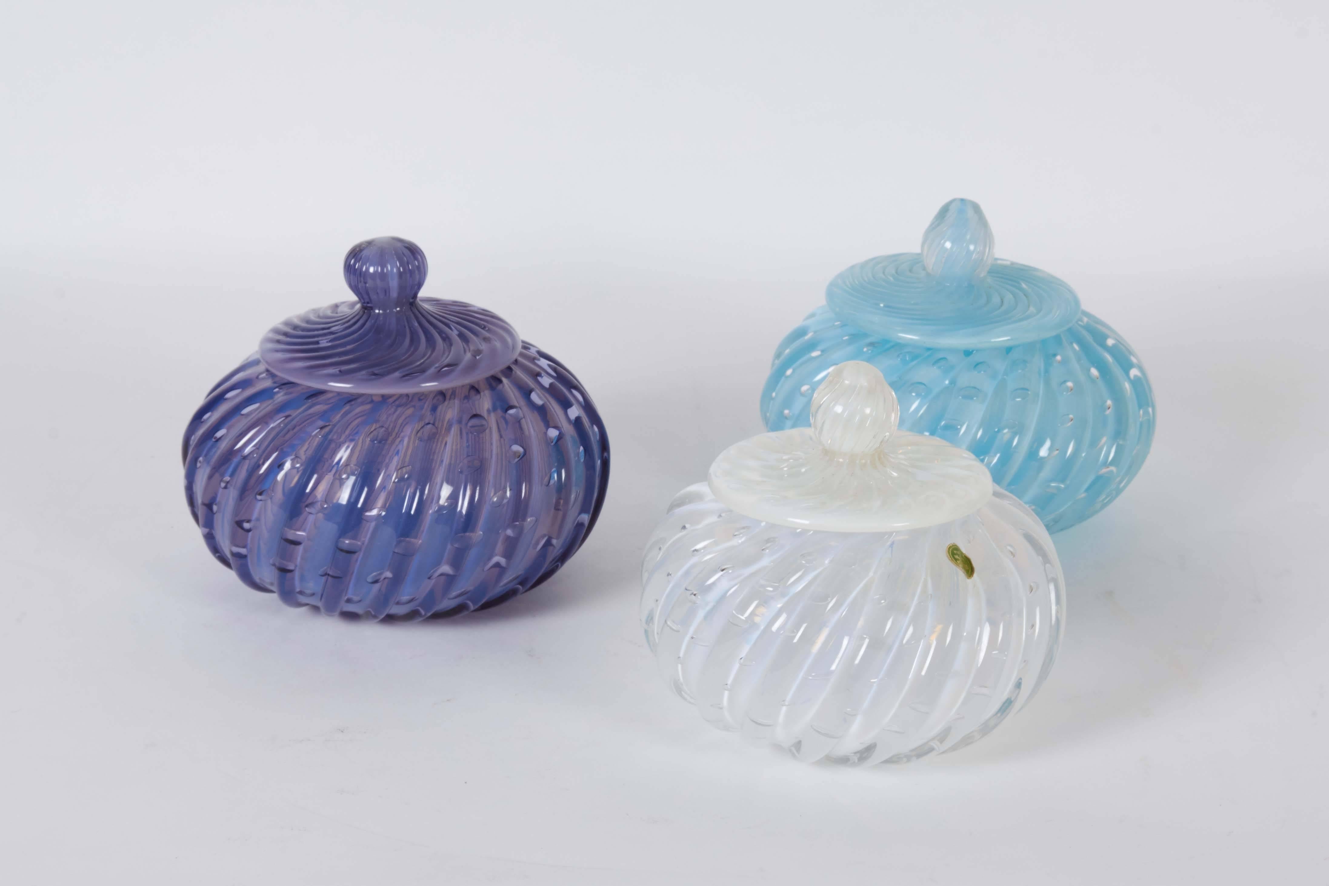 A set of three covered vanity jars, produced in Murano, Italy, circa 1950s by Seguso, in indigo, white and light blue blown ribbed glass, each with opalescent sheen and decorative 'bullicante' controlled bubbles. Markings include two sticker labels,