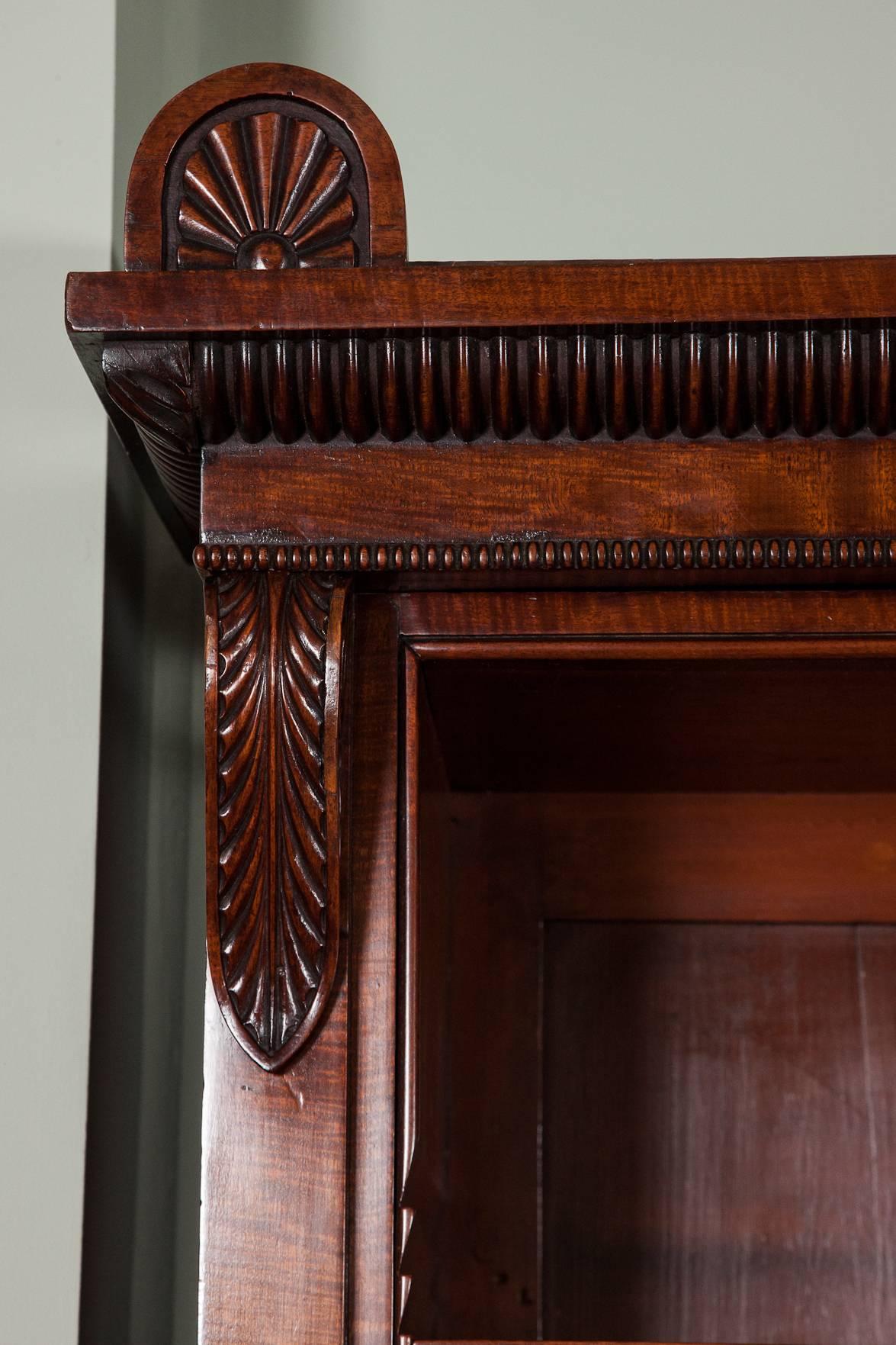 A George IV mahogany open bookcase, circa 1825, the cornice with central scroll and shell decoration above beaded edge and central double and flanking single bookcases with decorative corbels, on a bead moulded plinth base.
