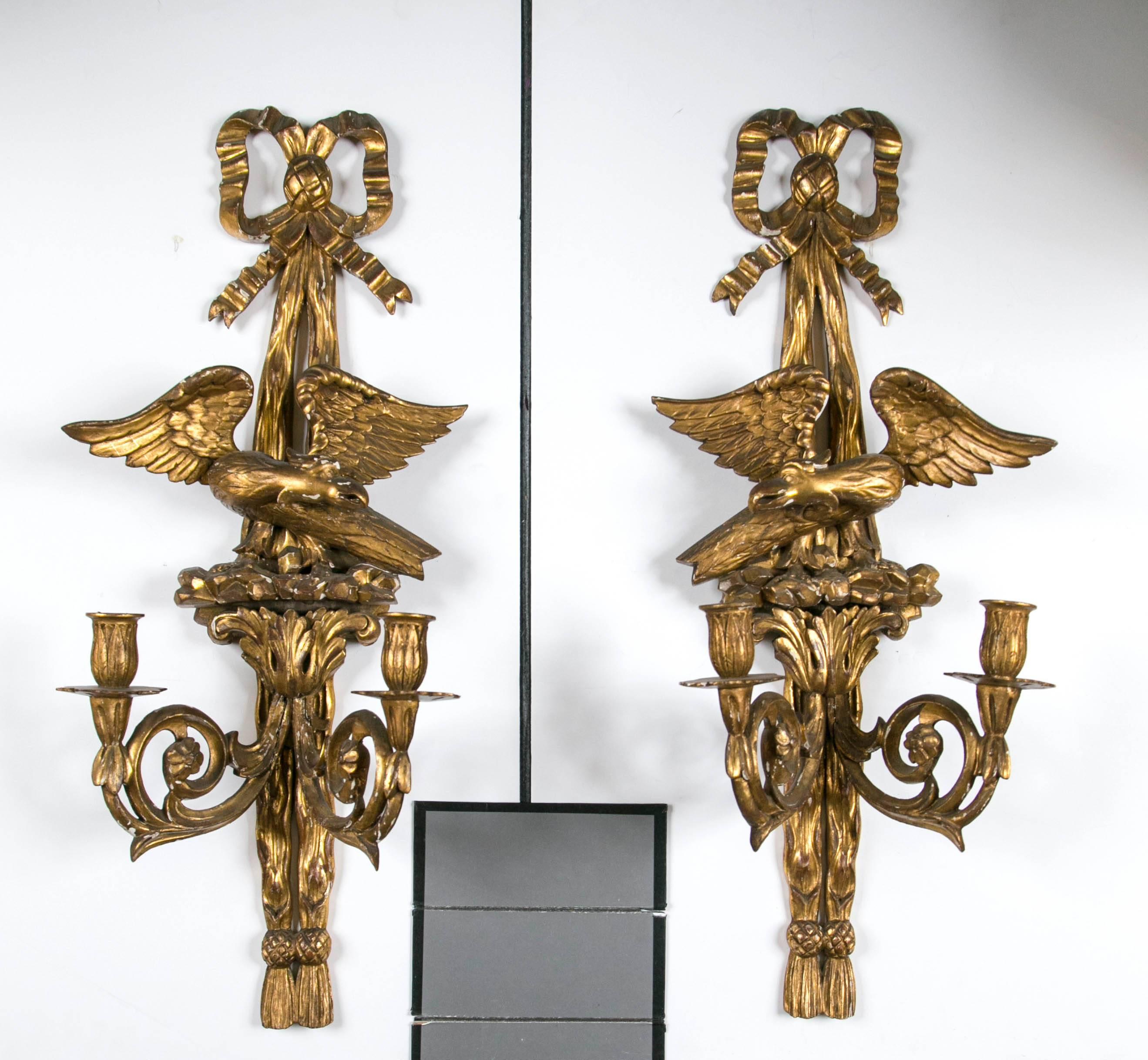 A wonderful pair of giltwood sconces topped with a Louis XVI style bow above an eagle with spread wings sitting on a rocky outcropping. The eagles are a true pair, one facing left, one facing right. Below is a scrolling acanthus leaf capital with