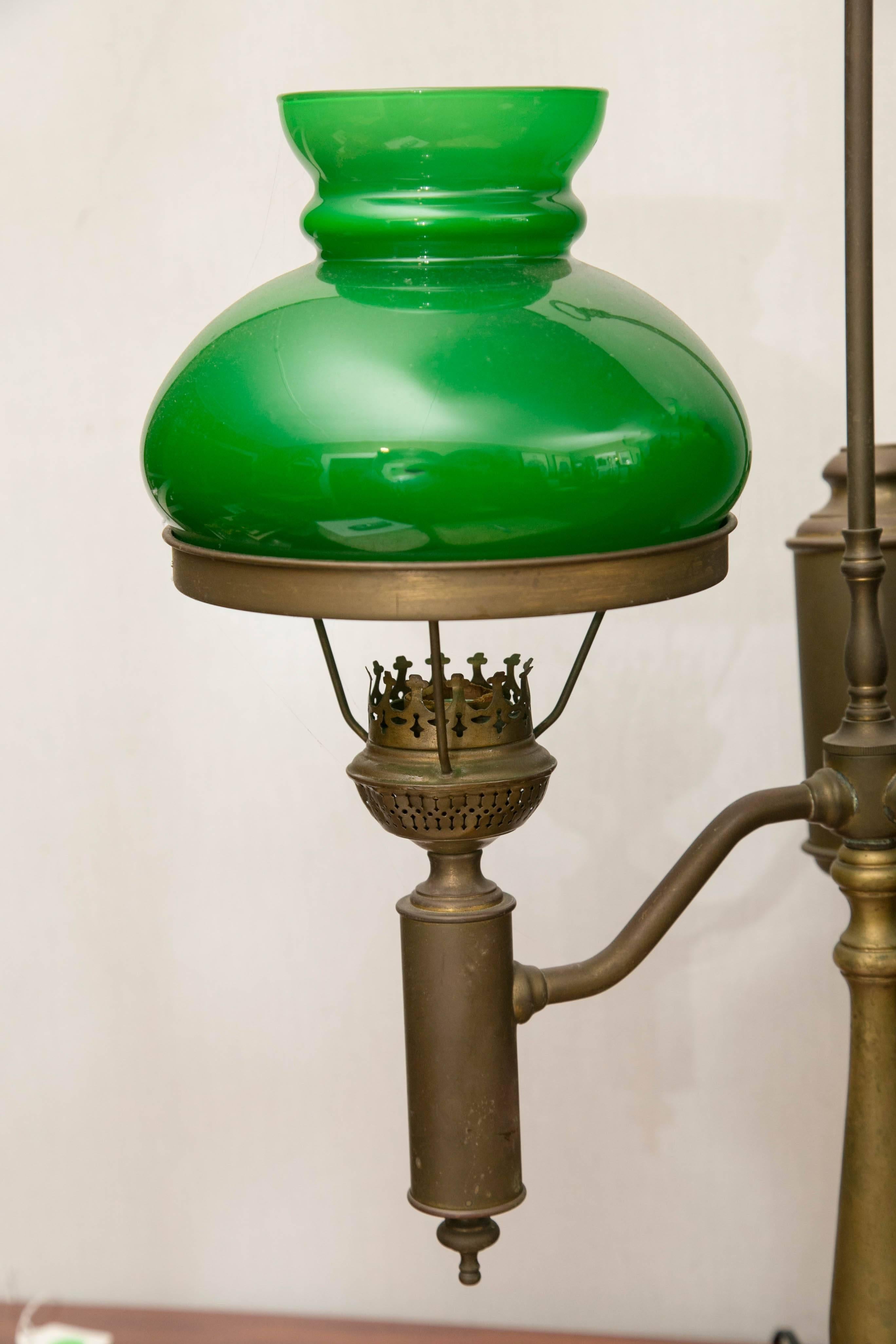 This lamp, made of solid brass was originally a gravity fed fuel lamp. It probably used kerosene. Today it is wired for electricity and is in working order. The two green glass case shades. With white interiors are in perfect condition. Neither the