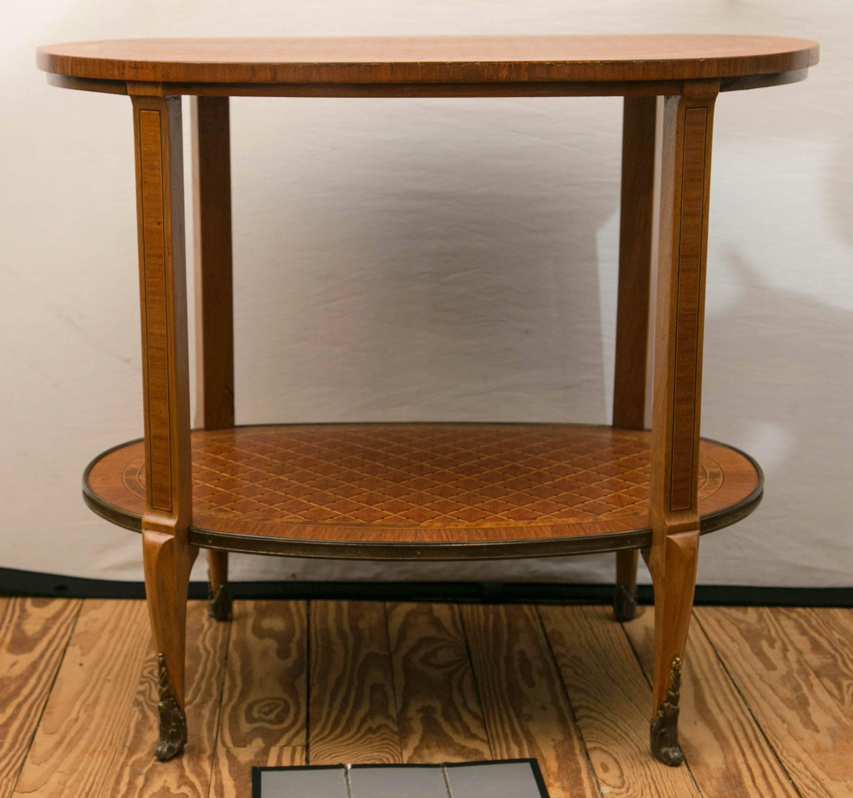 A fine reproduction two-tier oval side or end table. It is hand veneered parquetry with criss-crossing line of dark and light satinwood and ebony dots. The lower tier having a brass edge. Transitional style short legs ending in brass sabots.
