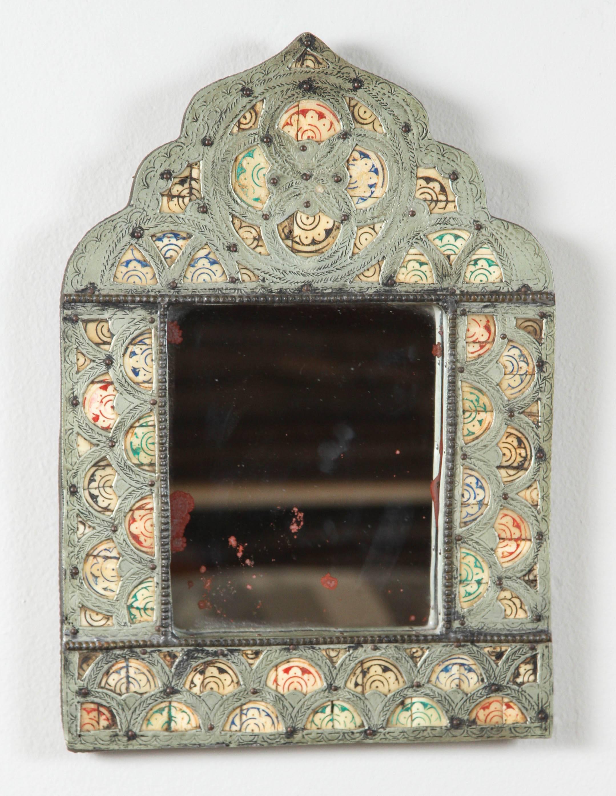 Incised metal over wood with painted insets. Red, green, black and blue. Leather back. Mirror shows signs of age with distressed sections.