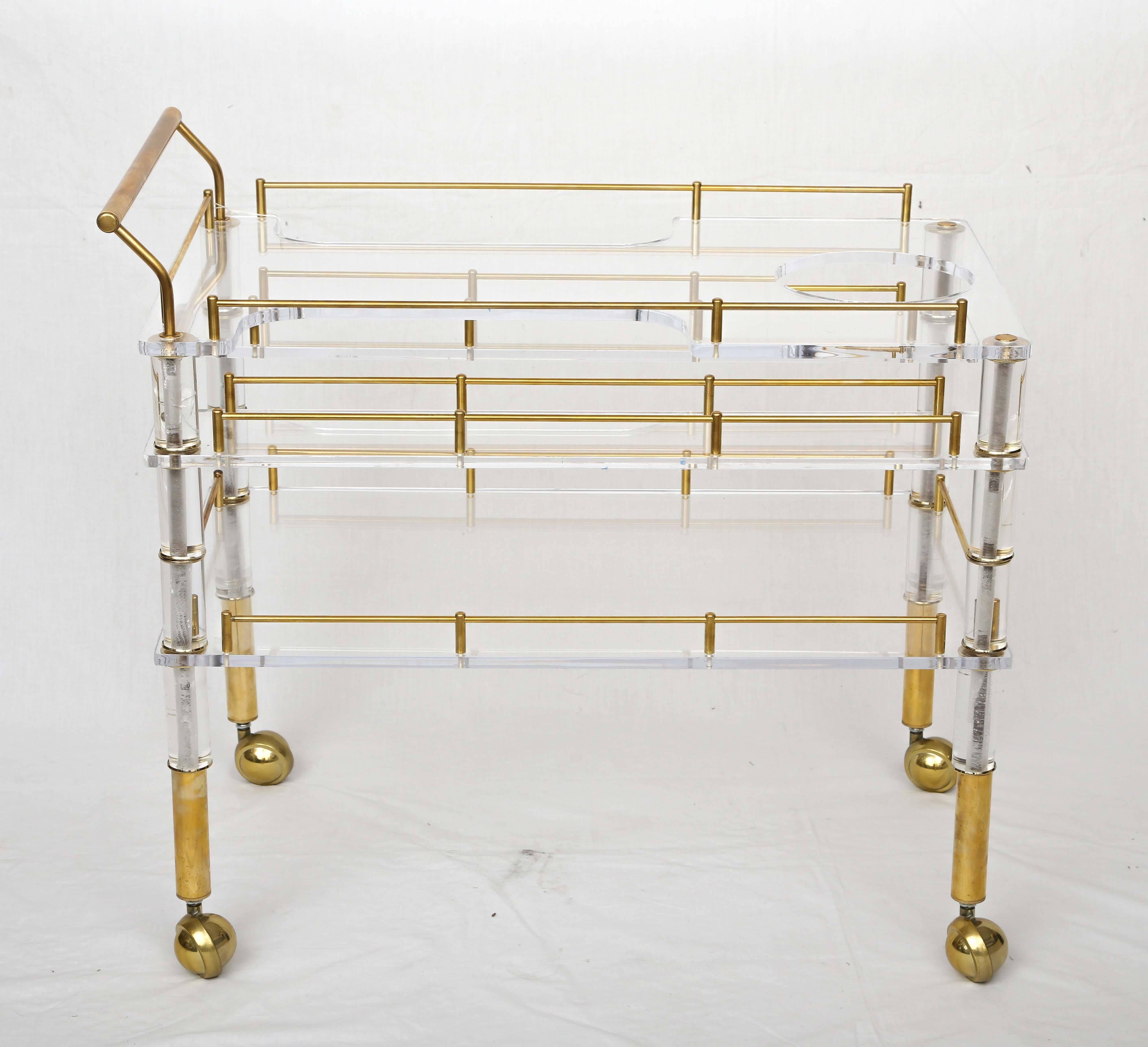 Offered is a beautiful crafted Lucite and brass bar cart on casters in the style of Charles Hollis Jones. It has two levels and the top can hold an ice bucket as well as drinking glasses on each side.
Note the brass details all around the cart.