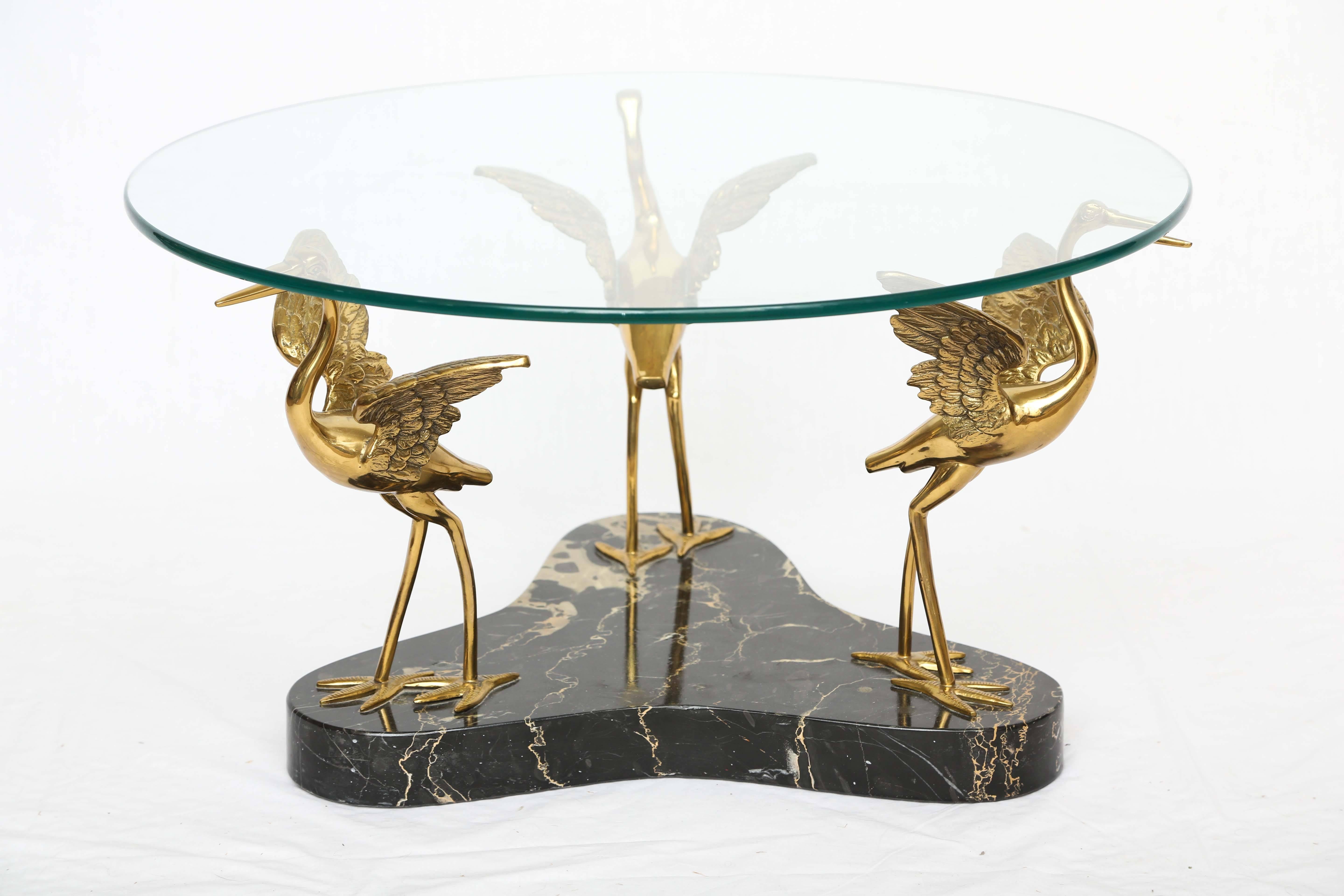 We offer a marble and brass birds coffee table in the style of Willy Daro. The birds are made with great craftsmanship and the base is black marble with a unique pattern.
The round glass top sits on the beaks of the birds.