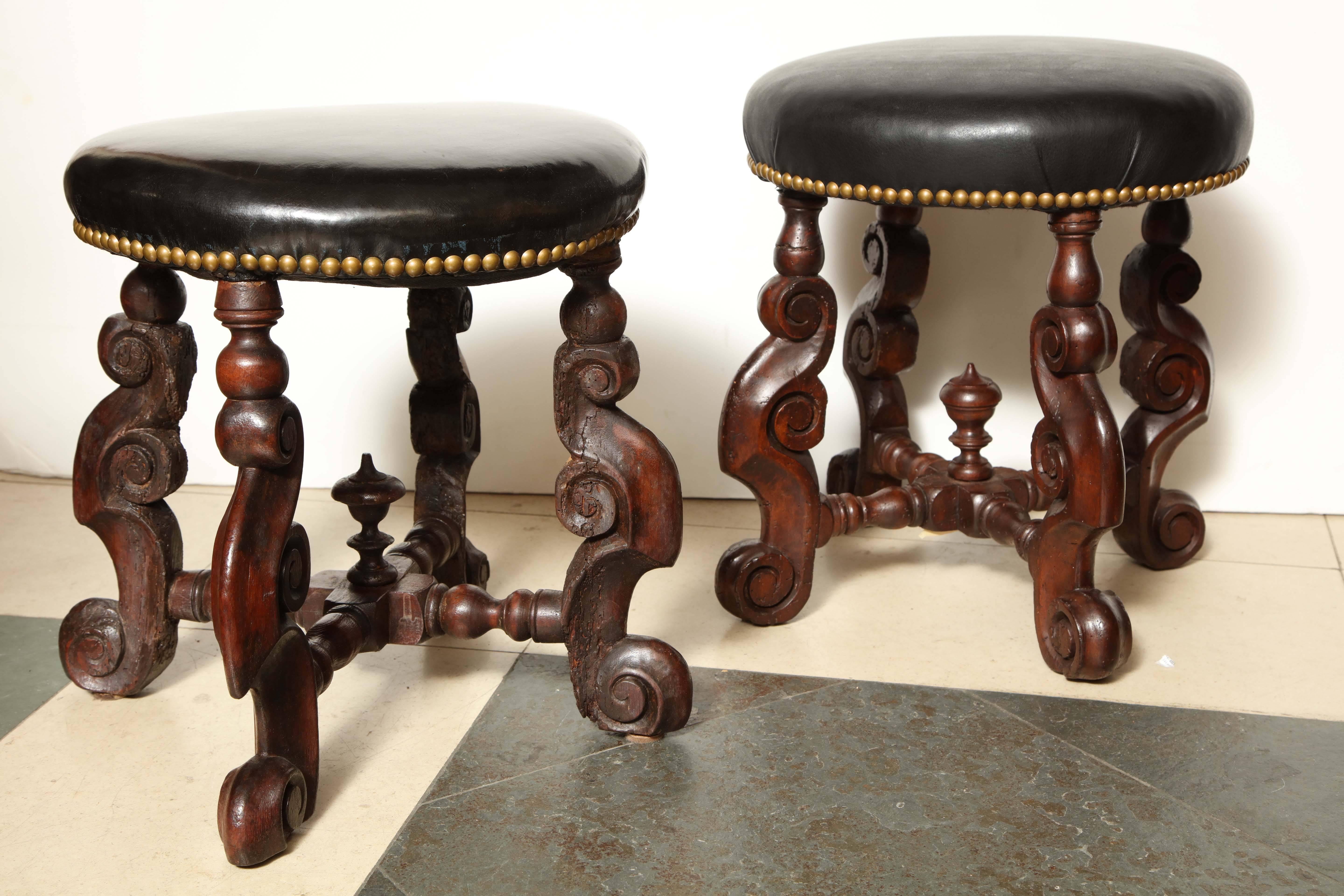 A rare pair of William and Mary carved walnut stools with round leather upholstered cushions.