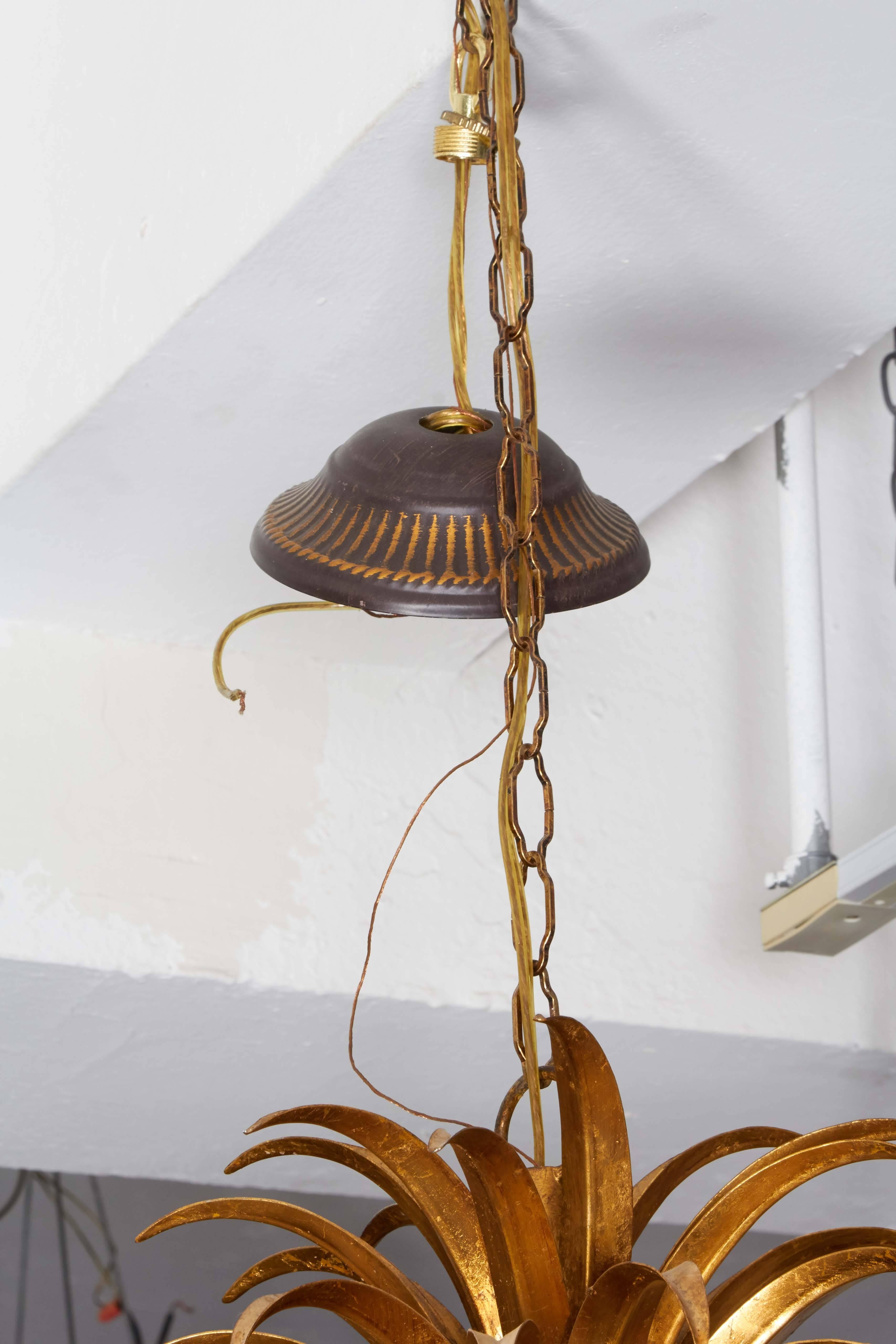 A Hollywood Regency style gilt tole metal chandelier, produced circa 1960s, featuring a pineapple on leaves, bound by stylized rope, with eight curved arms, each with decorative floral bobeche. Very good vintage condition, wear consistent with age