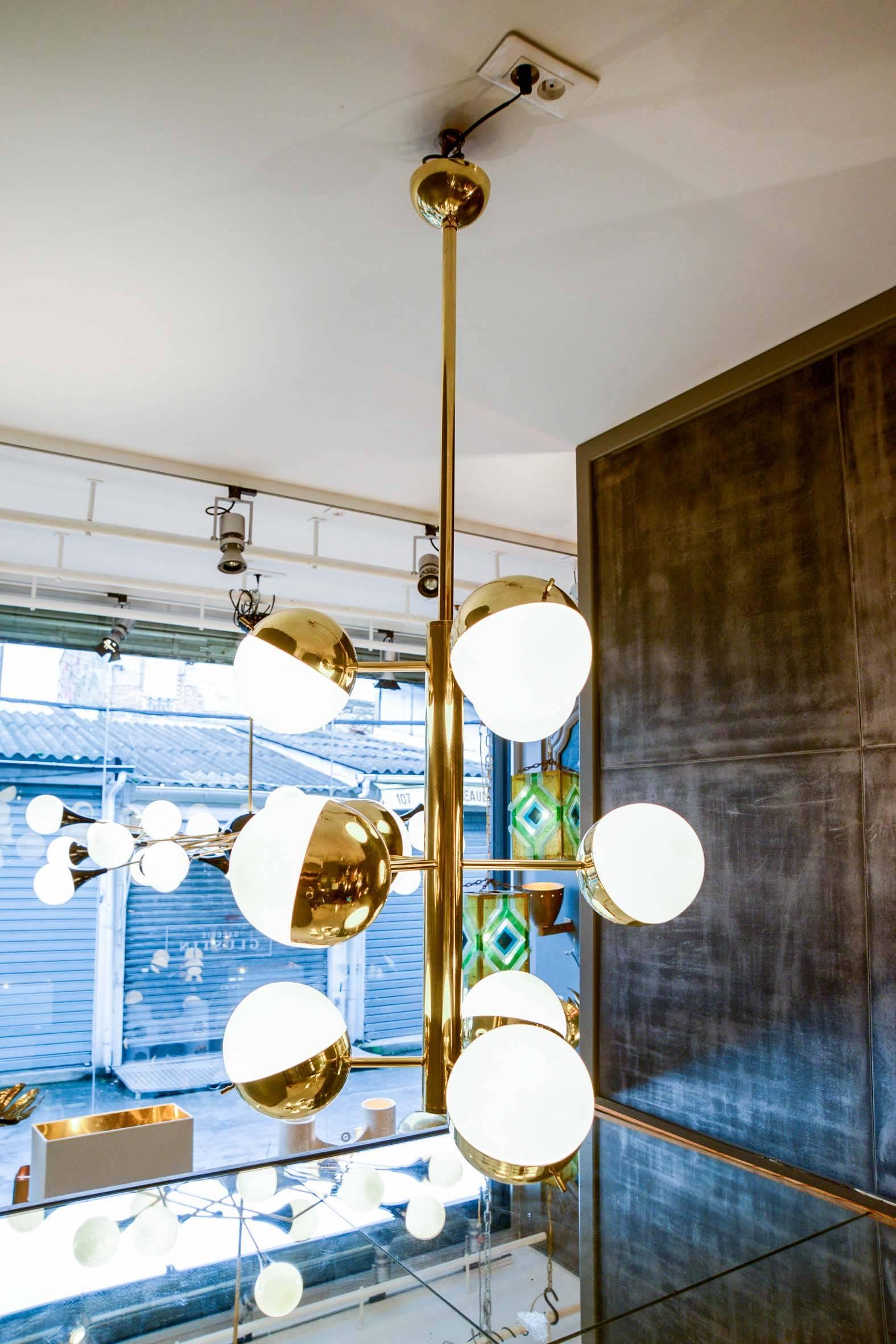 Tall suspension made of shiny brass with three levels of lights, hidden in a half brass and half glass sphere.