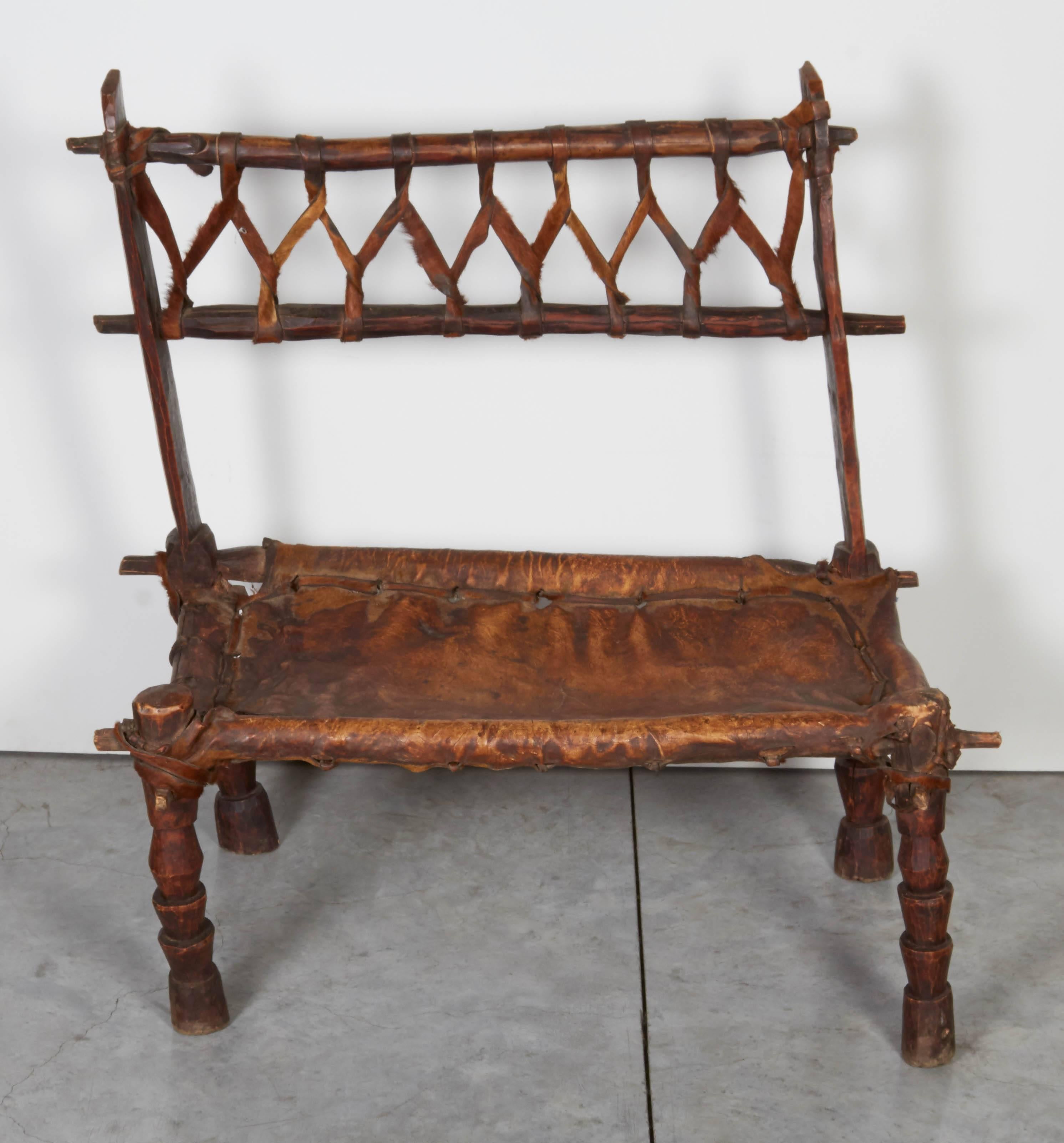 A simple, quirky, rustic wooden bench with a beautifully worn leather seat and crosshatch leather back. This antique low bench from Ethiopia looks great from any angle and has great presence. 
CH370.