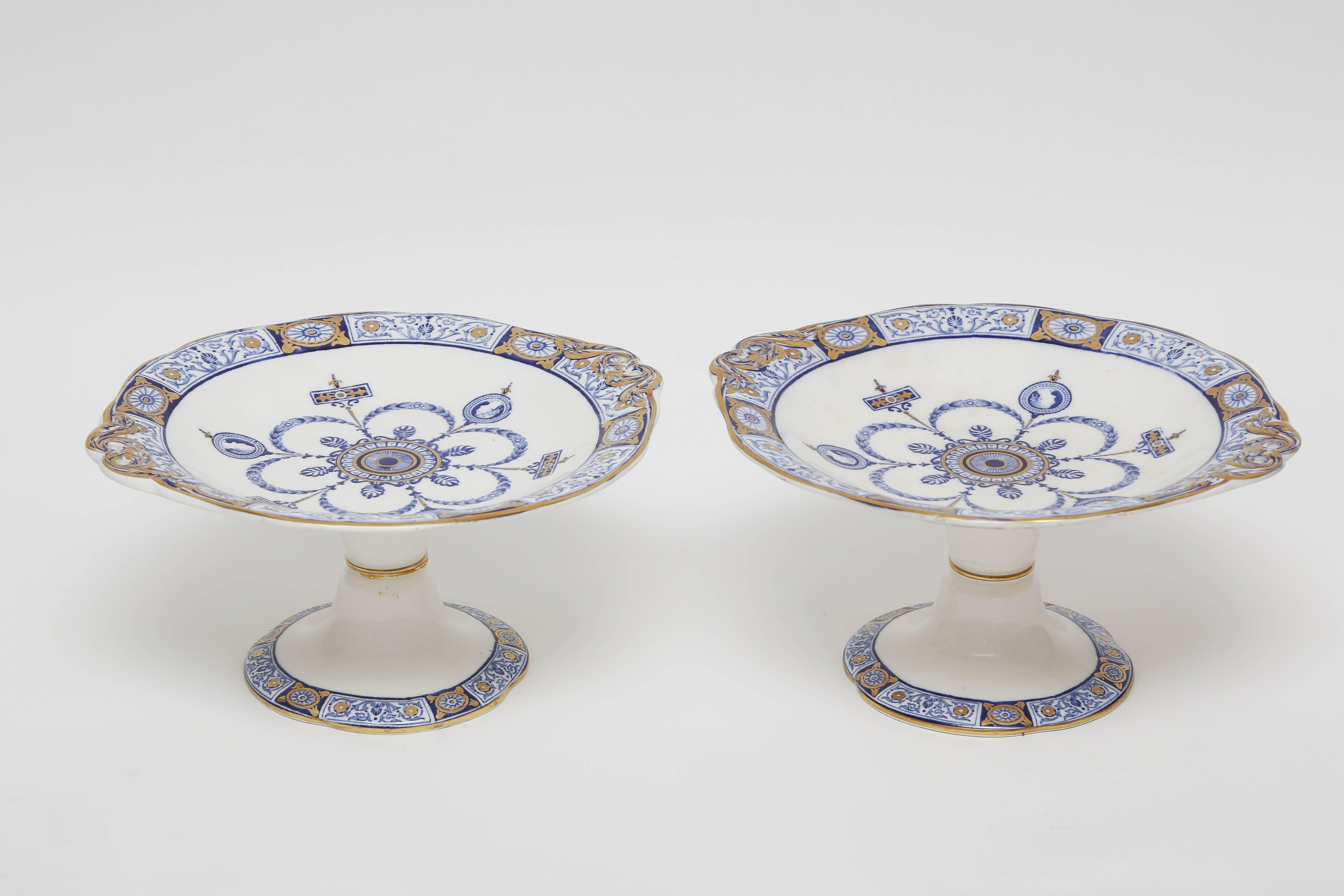 A Classic and elegant pair of tall pedestal based fruit or dessert compotes in a striking blue and white pattern. This design features figural Greco Roman portraits and an Aesthetic Movement central medallion. Hand gilt in 24-karat and in very nice