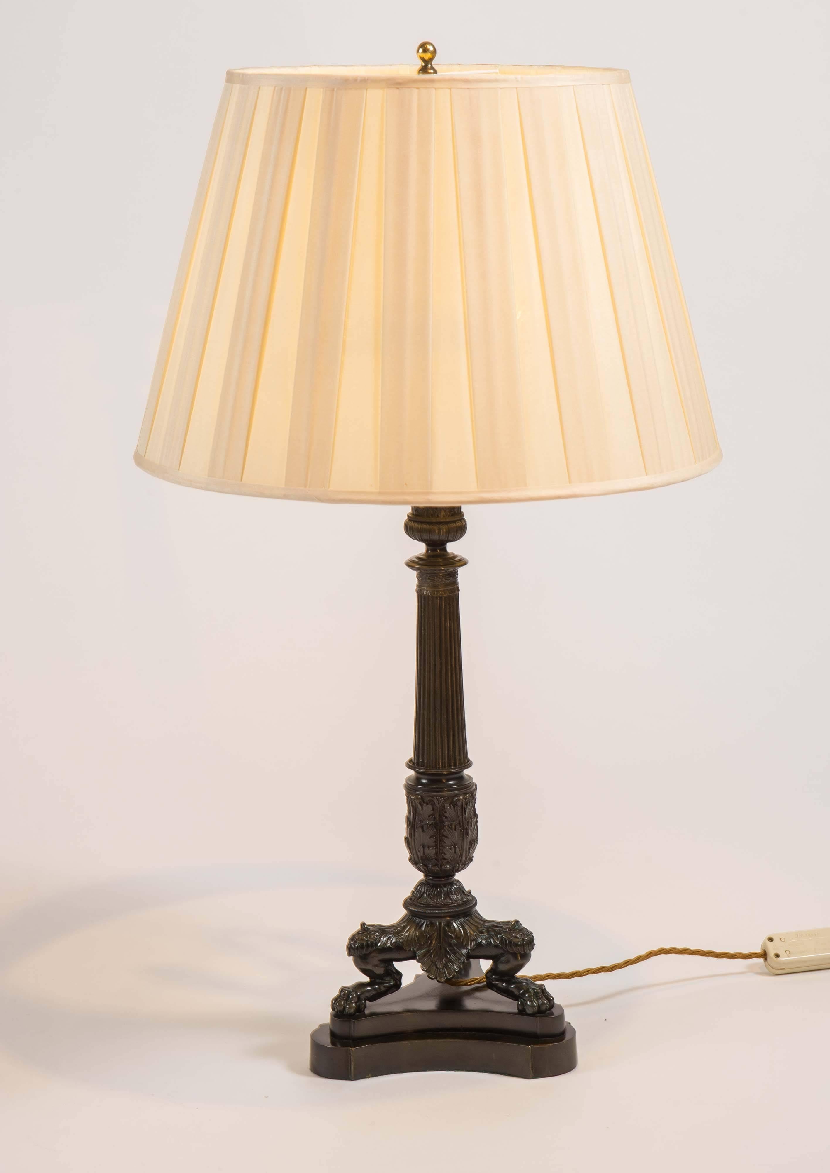 With reeded columns and paw feet on triform bases. This pair of table lamps are particularly well cast and have a wonderful dark green antiques patina; the custom-made cream pleated silk shades with height adjustable support. The lamp bases 19