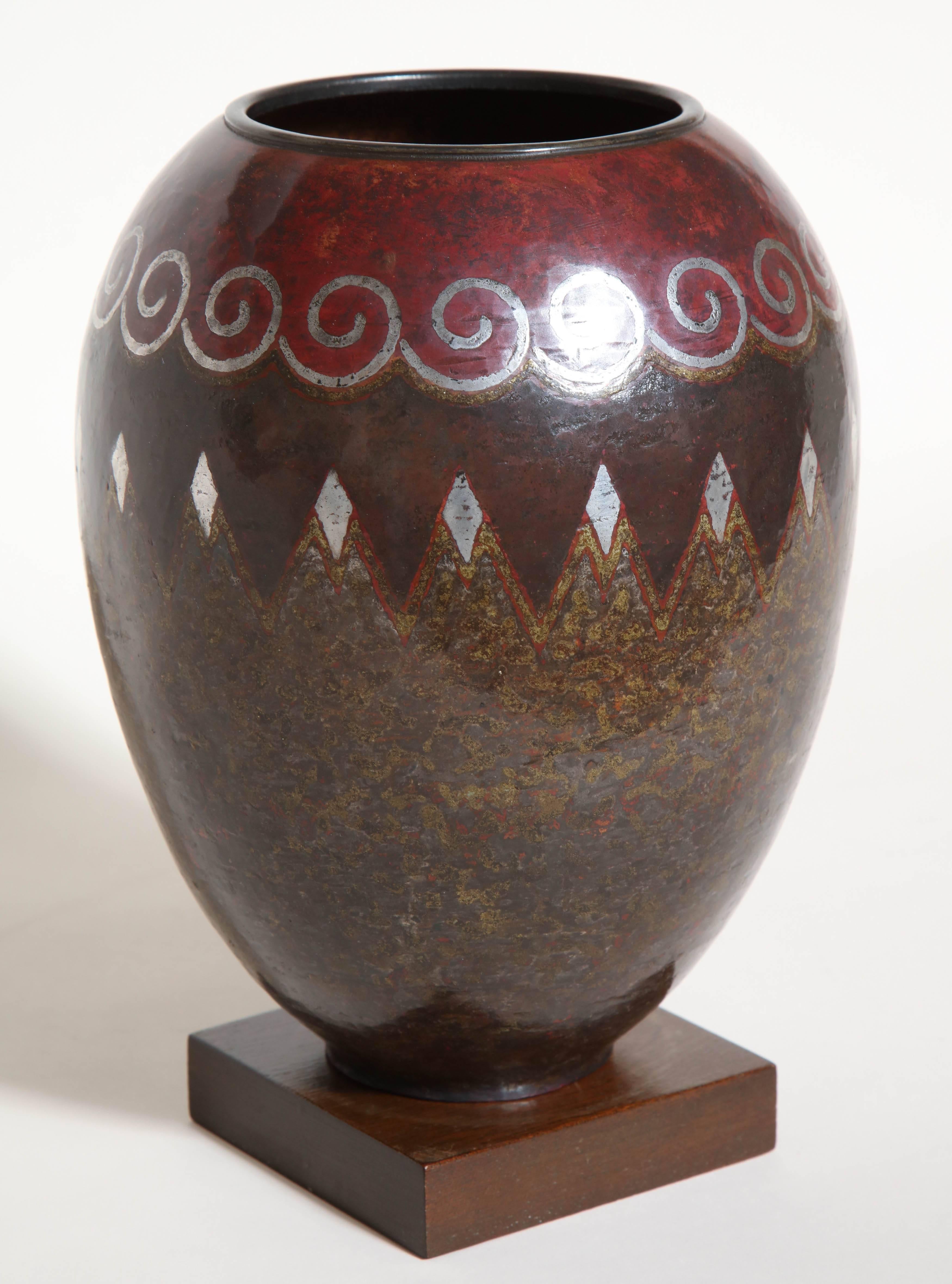 8 3/4'' high; 6 7/8'' wide
9 1/2'' high on oak base

This tall ovoid vase with annular collar has fired patina and silver inlays on a background, also patinated with fire, red in the upper part and pebbled jasper in the lower part. The vase has a