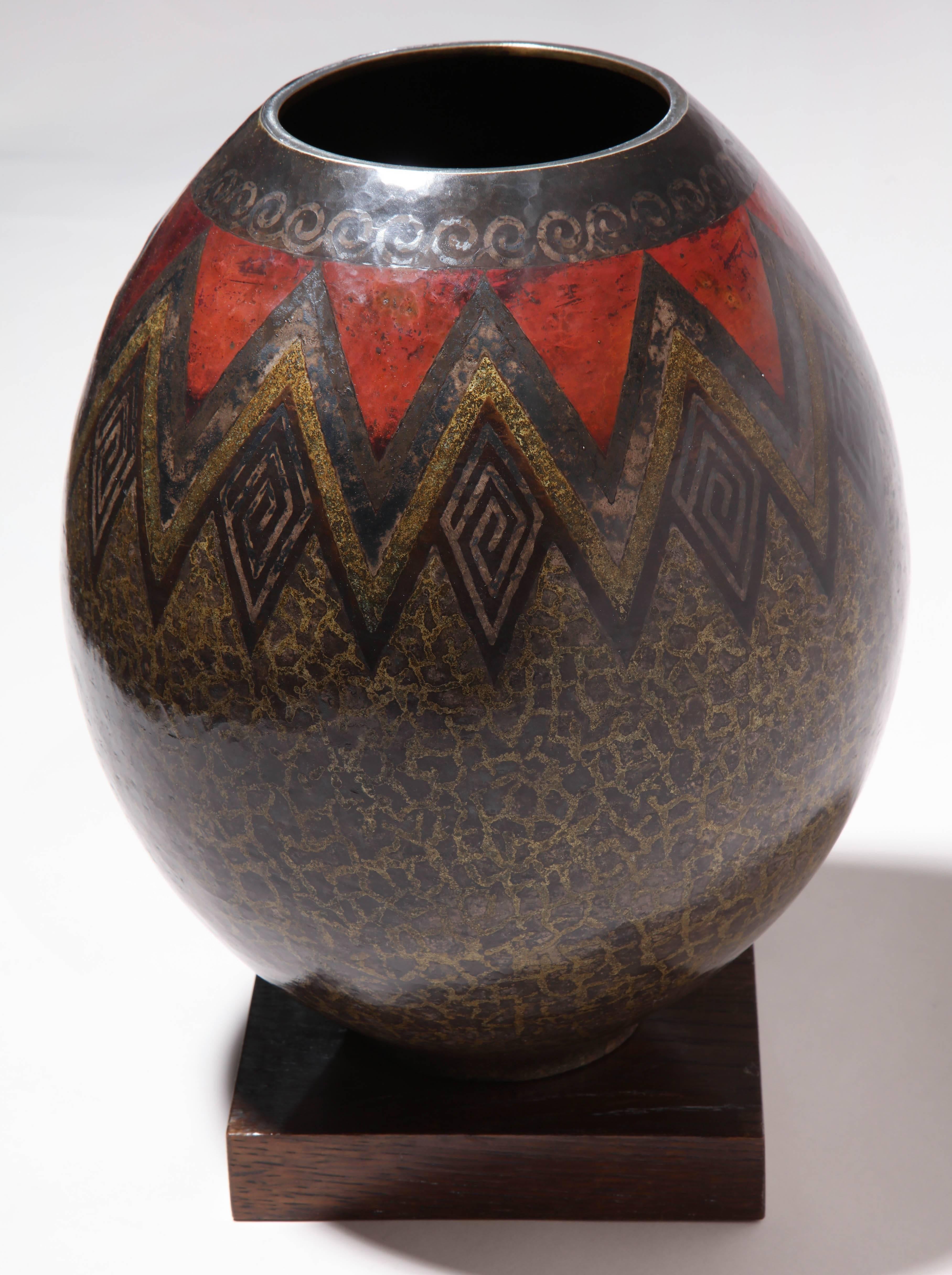 This exceptional and important ovoid vase is decorated with fired patina and silver inlays on a background, also patinated with fire, red and anthracite in the upper part and vermiculated in the lower part. It sits on its original oak base, probably