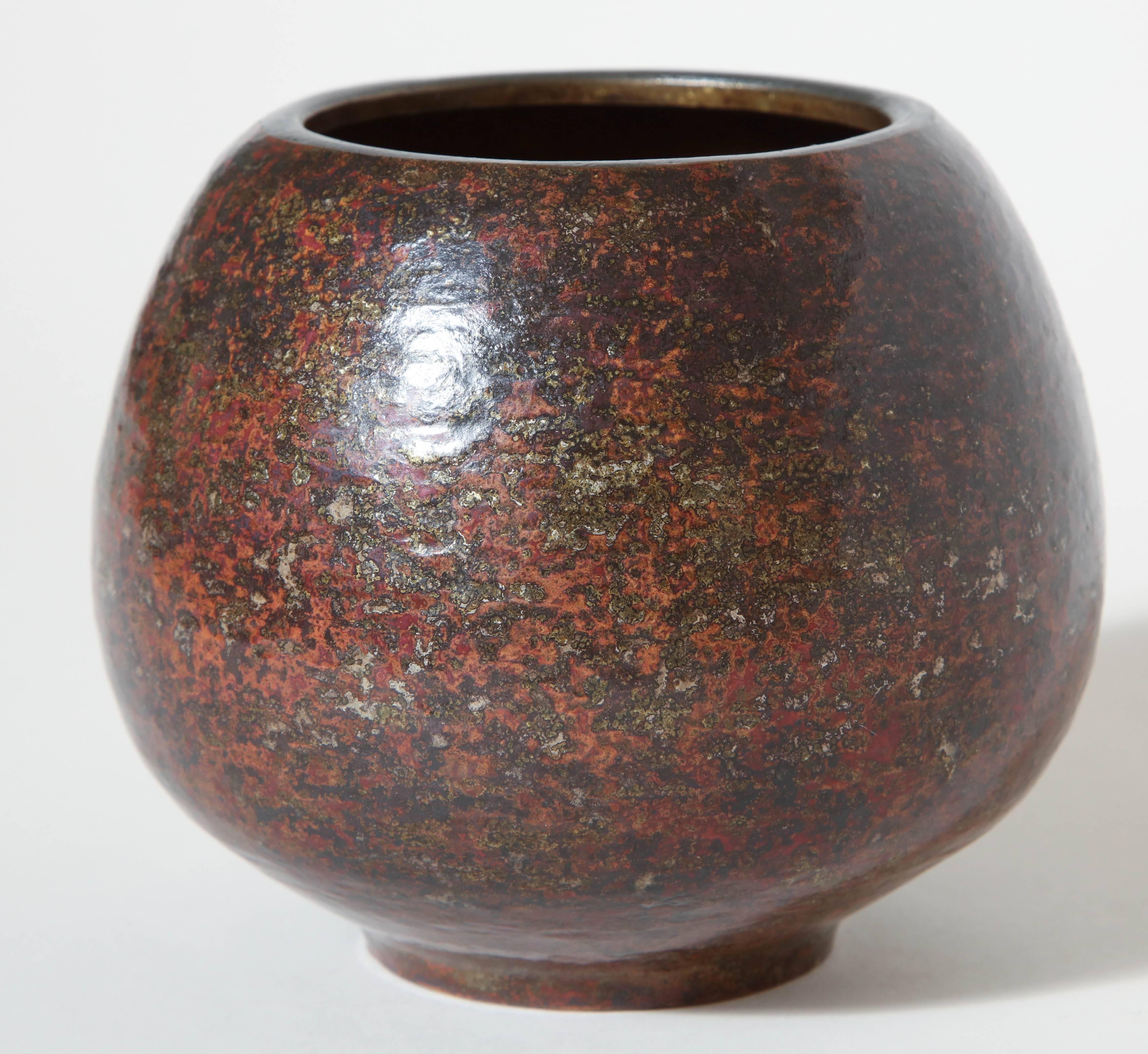 This ovoid vase with a wide annular collar has decoration made with a fired patina and inlays of silver on background, also patinated with fire, coral and gray anthracite. This gives an overall pebbled jasper appearance. 

Inscribed 
