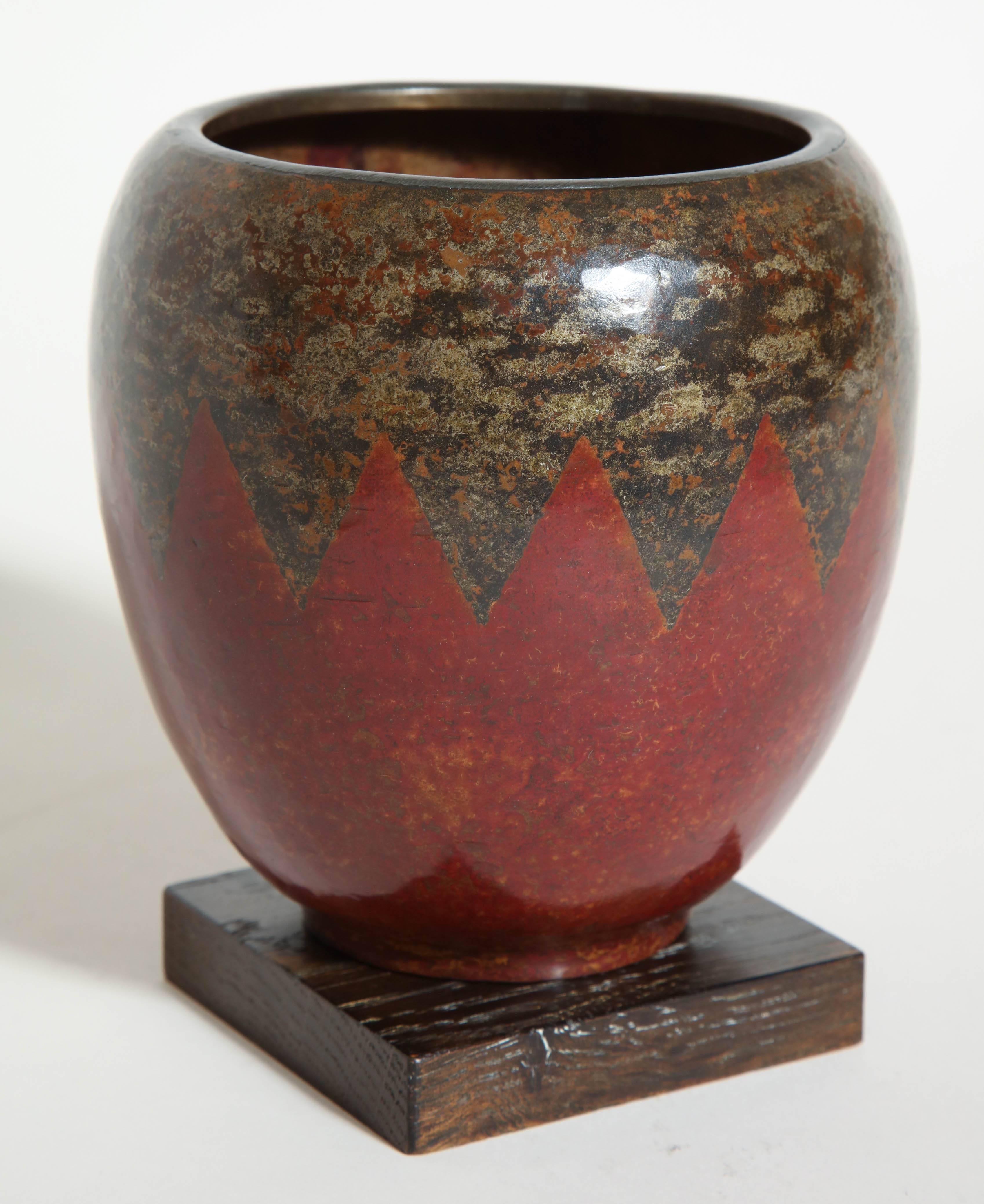Measures: 4 7/8'' high; 4 7/8'' wide
5 1/2'' high on oak base

This ovoid vase with a large annular collar is patinated with fire and has inlays of silver on triangles pointing down, also patinated with fire. The lower section is intense red.