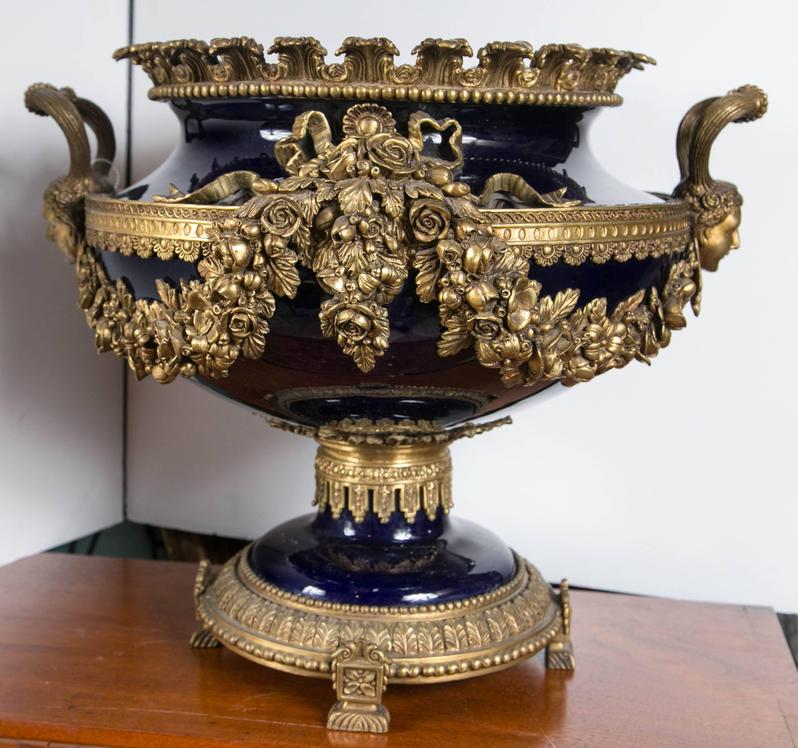 Dramatic urn form center piece with bronze mounts and handles. Faces oon the handles and swags of floral garlands.

shipping cost is an approximate.