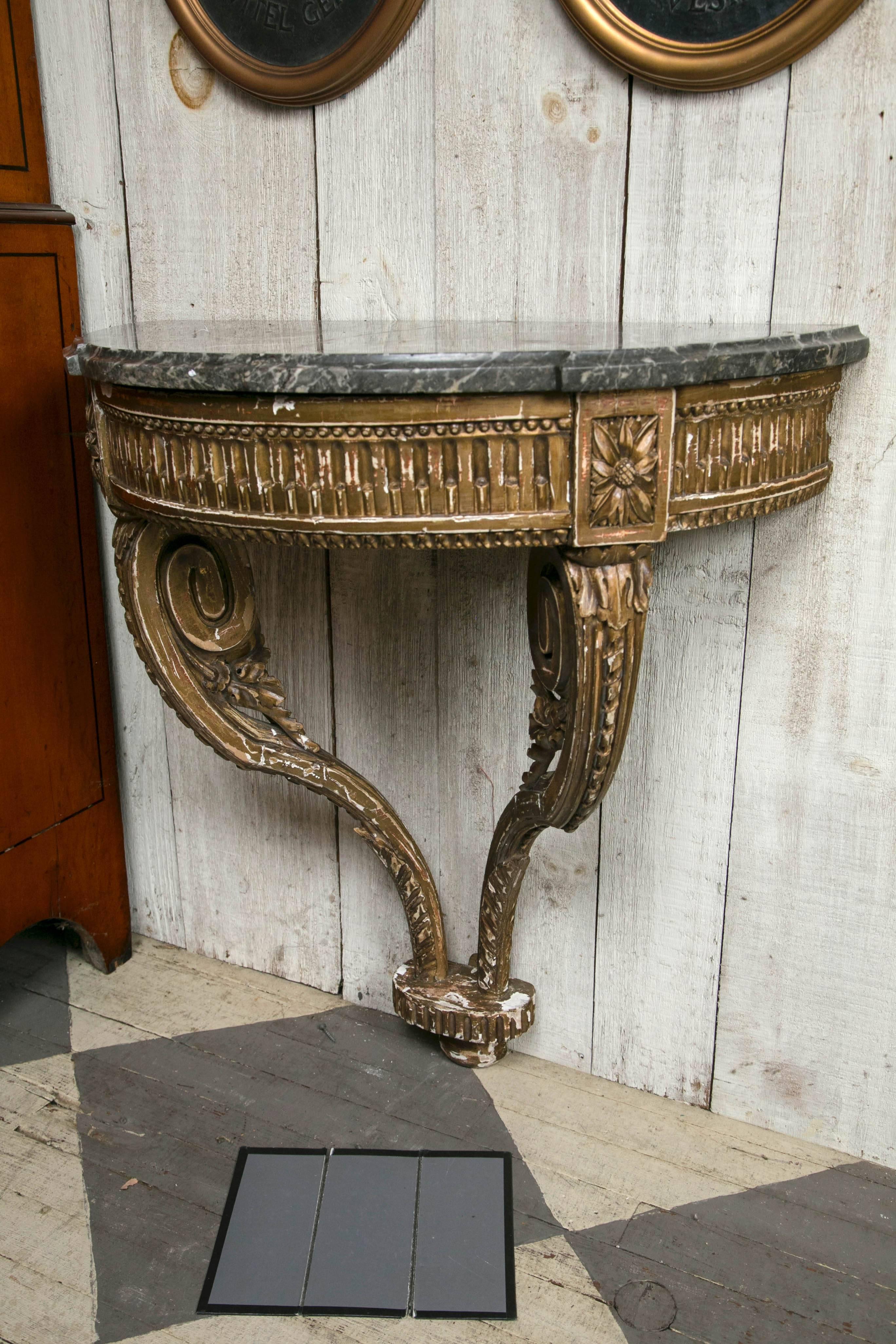 This D-shaped console is made to be attached to a wall. It is of the Louis XVI period.
 The top of grey with white marble has been repaired. Giltwood with a deeply carved apron and incurving legs.
Worn gilt exposing the white gesso.
 