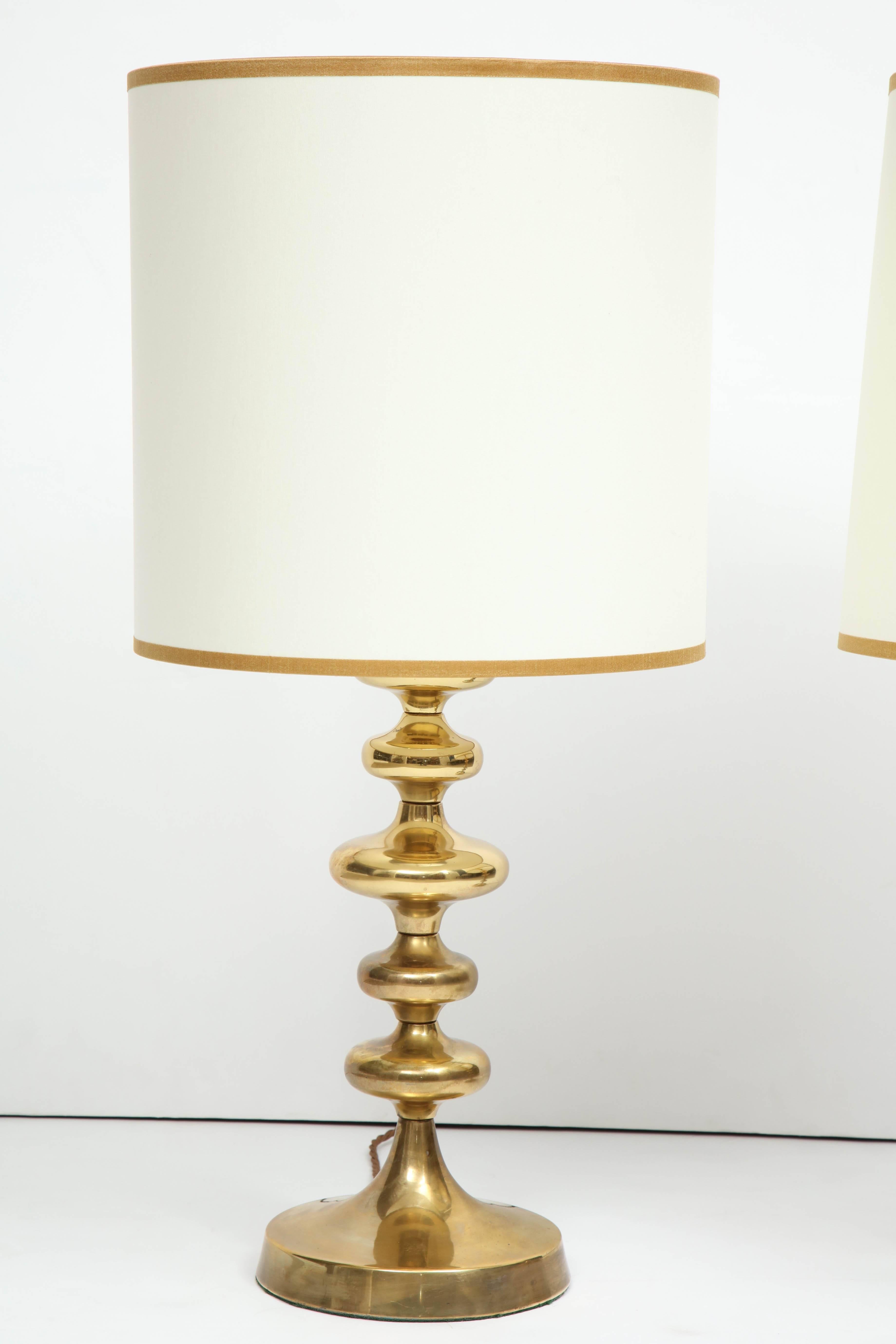 A pair of brass lamps made in Sweden, consisting of concentric turned shapes, and fitted with custom ivory cotton drum shades with metallic gold trim. Newly re-wired for use in the U.S.
 