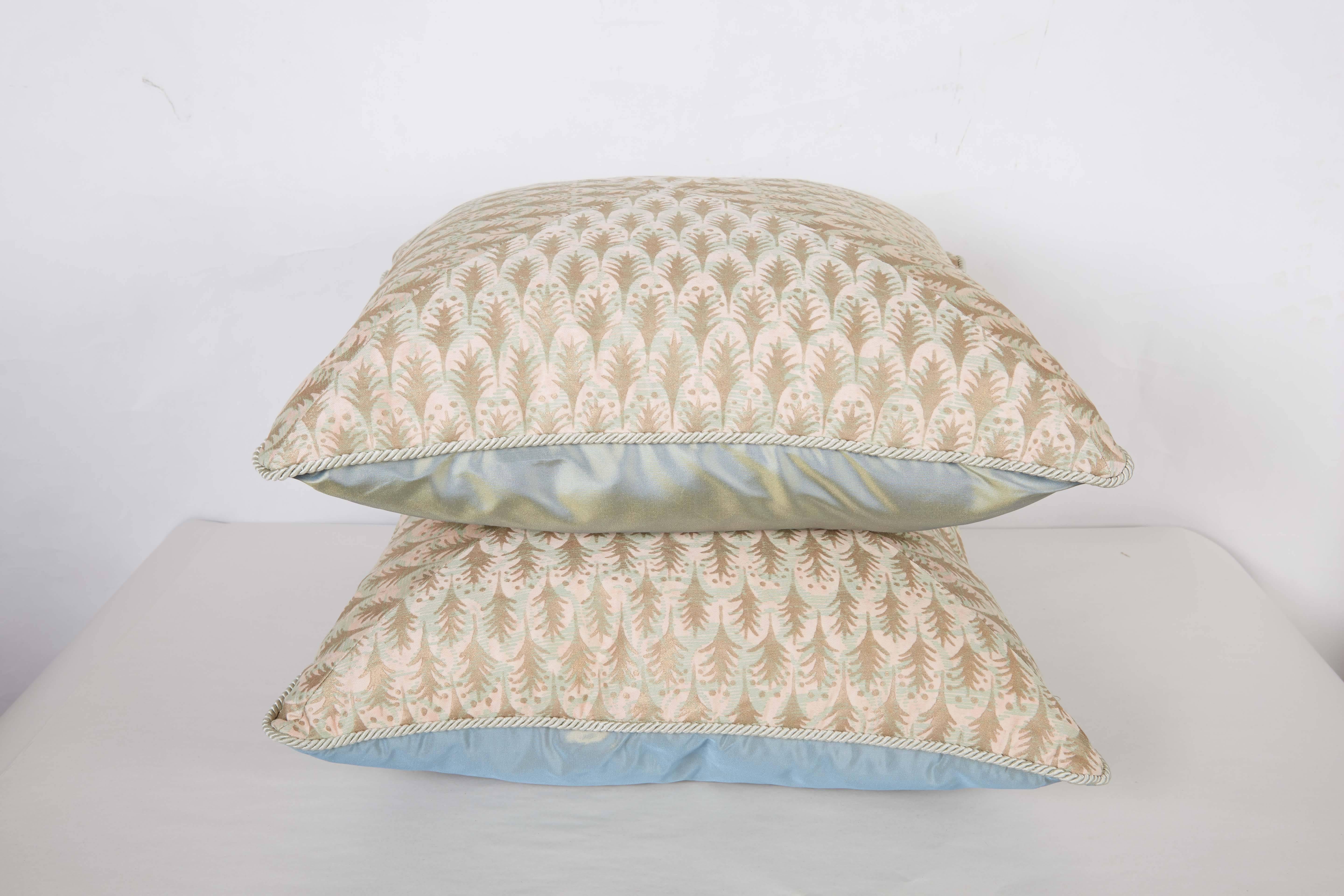 A pair of mitered  Fortuny fabric cushions in the Puimette pattern, pink, aquamarine and gold color way with braid trim and blue taffeta backing, the pattern, a 15th century Persian design with small feathers motif. Newly made.
50 down/50 feather