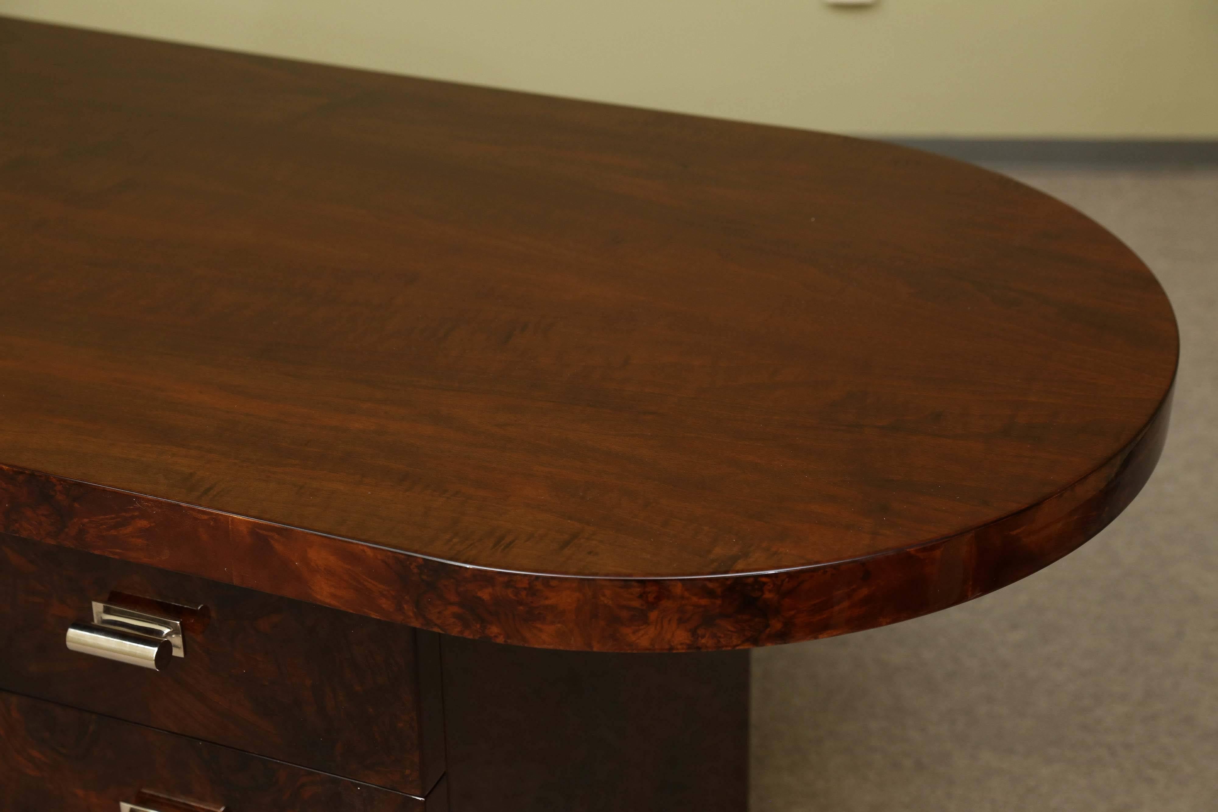 The desk is made out of fine walnut wood. It has a wide tabletop that displays the beauty of the wood. On the left side the tabletop has a round end on the right it is angular. The tabletop is supported by the four drawers on the left side and