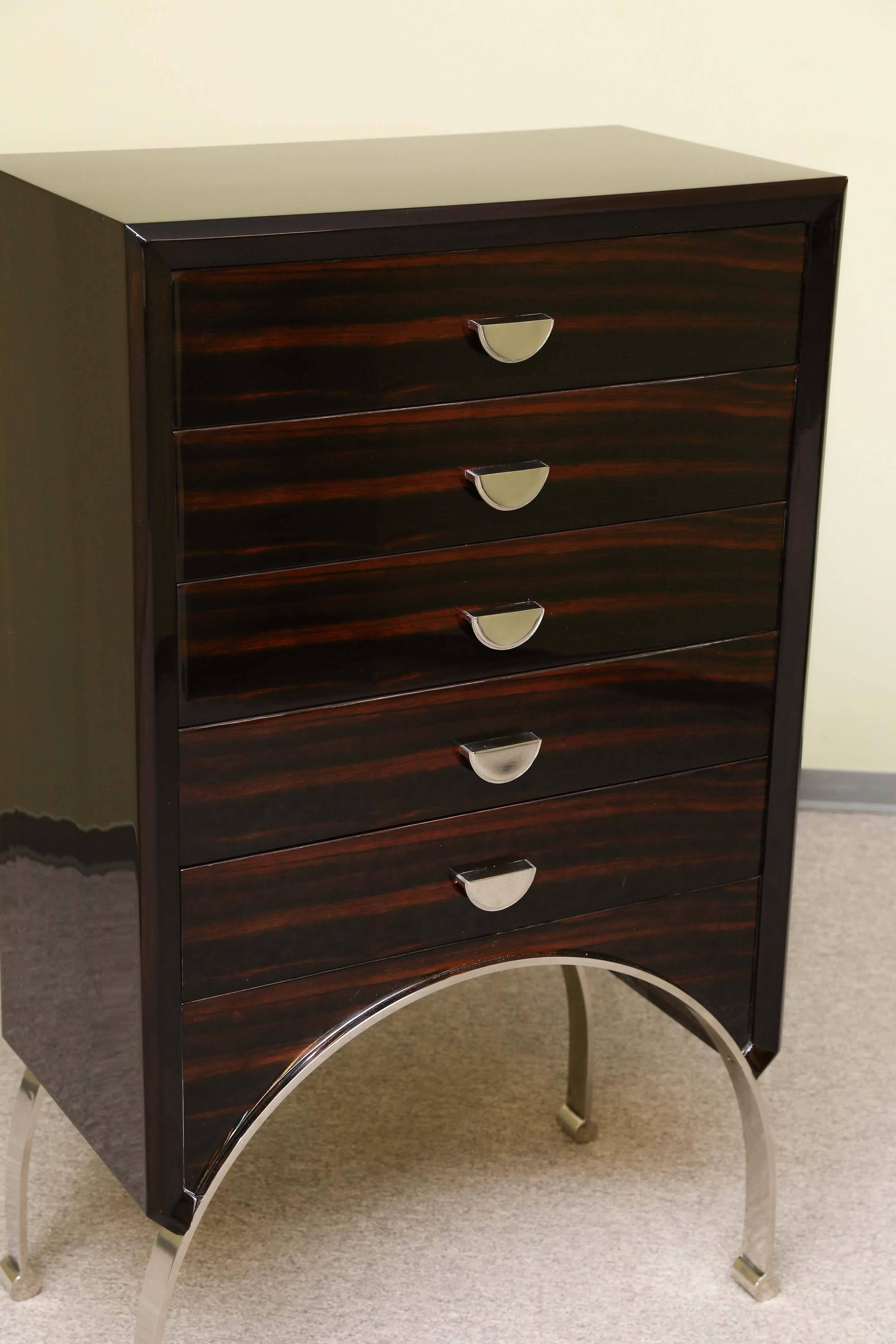 Chest of drawers is made out of two types of wood Macassar and walnut. It has five drawers with semi-circular chrome handles. It is elevated by four curvy chrome legs. Curvature of legs is transformed into the bottom of the chest, creating unusual