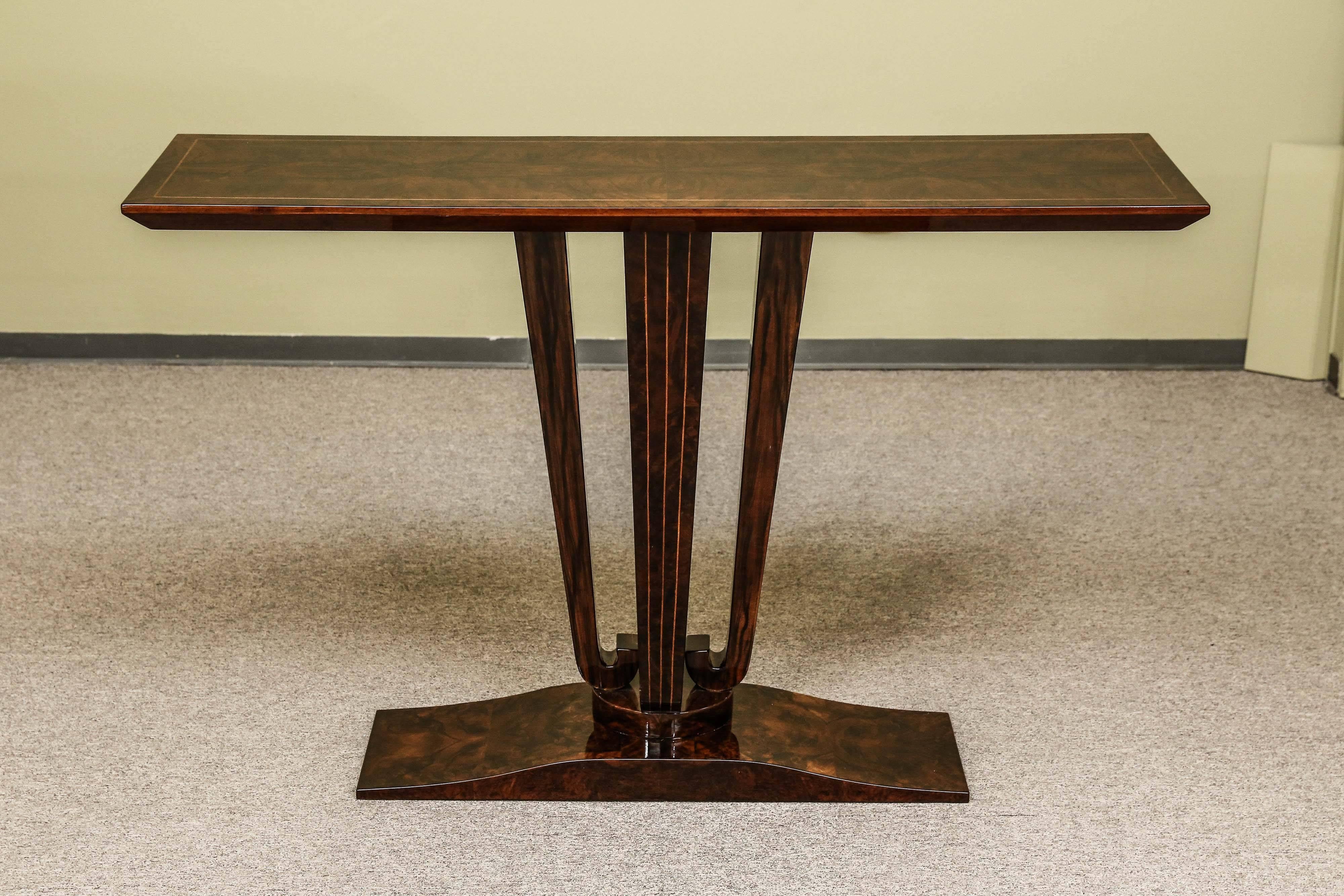 Rectangular top is elevated by the three legs, that are curved on the bottom and are connected to the trapezoidal base. Top of the table has inlaid trimming that is emphasizing corners of the console. Each one of the legs has three streaming down
